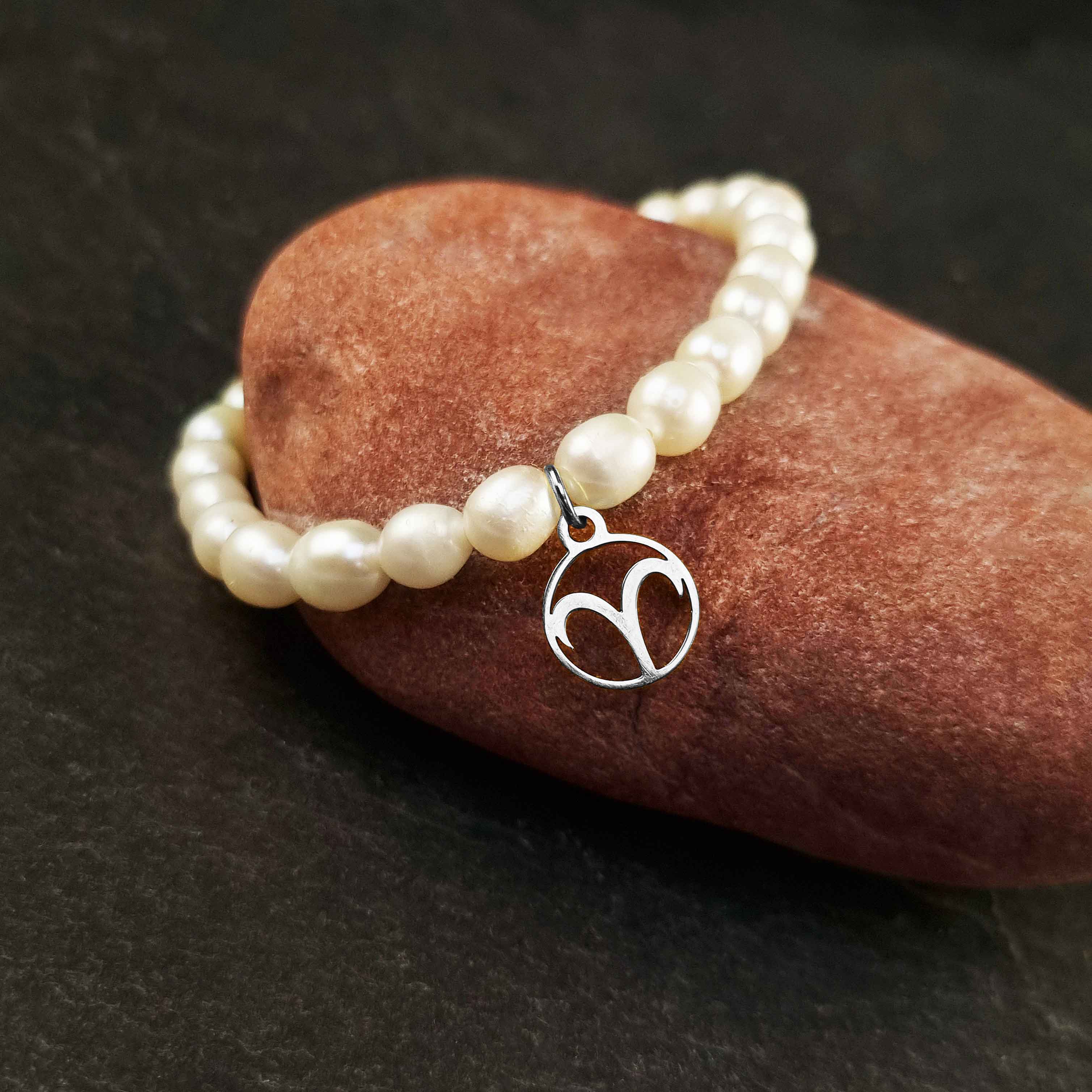 Wit zoetwater parel armband met zilveren symbool van sterrenbeeld Ram van edelstaal liggend op rode steen | Zilveren sterrenbeeld Ram