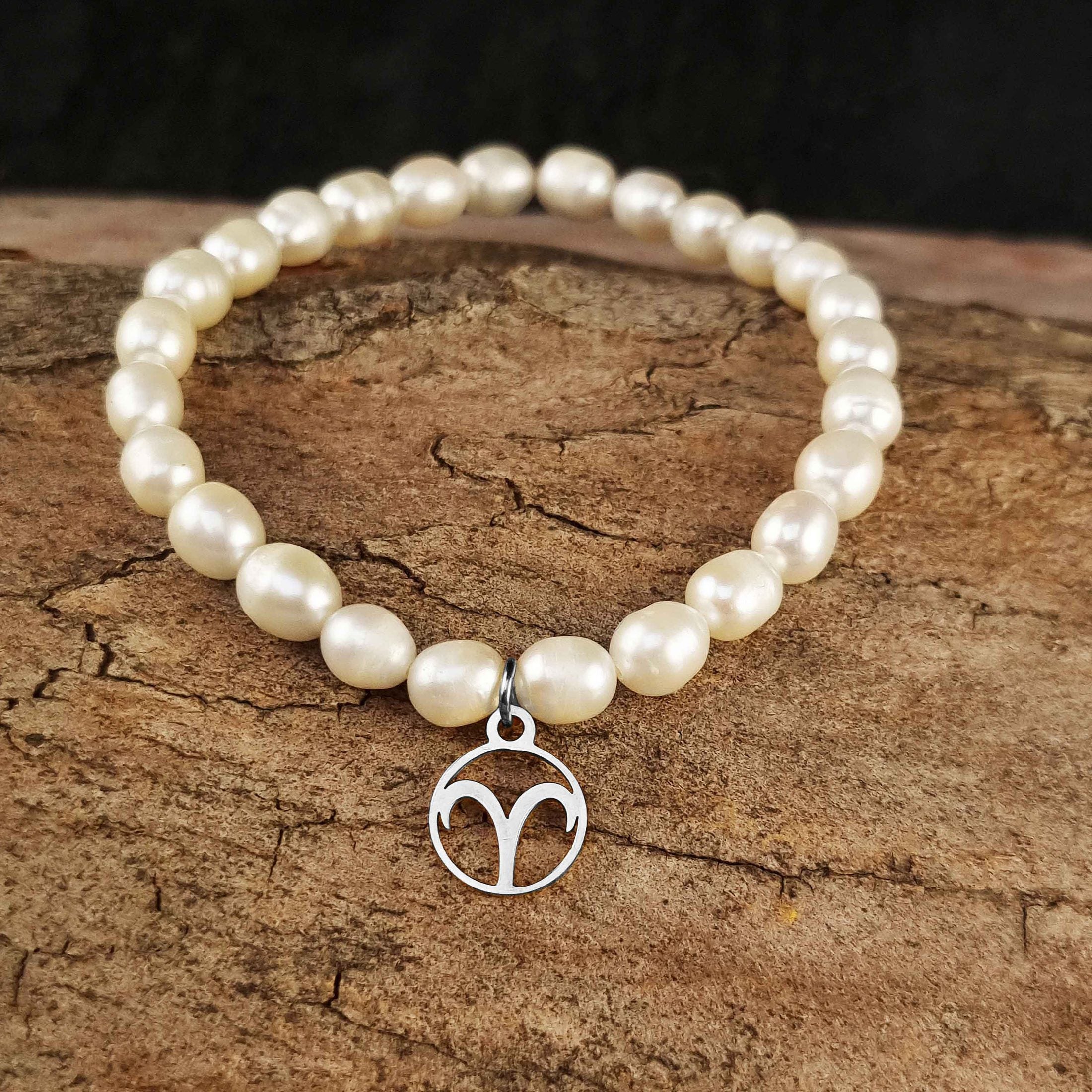 Wit zoetwater parel armband met zilveren symbool van sterrenbeeld Ram van edelstaal liggend op hout | Zilveren sterrenbeeld Ram