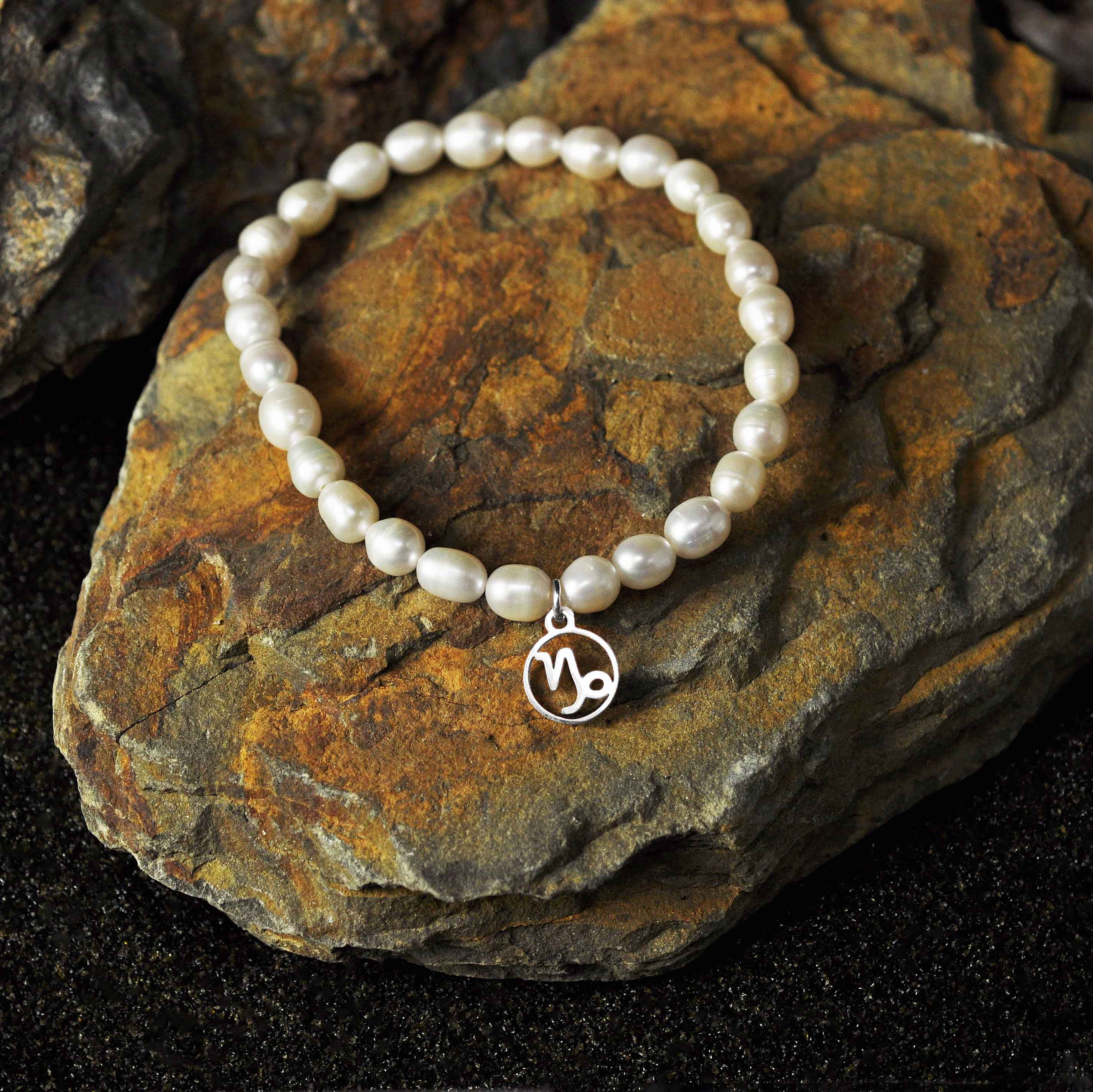 Wit zoetwater parel armband met zilver edelstalen symbool sterrenbeeld steenbok liggend op steen | Parel armband Zilveren Sterrenbeeld Steenbok