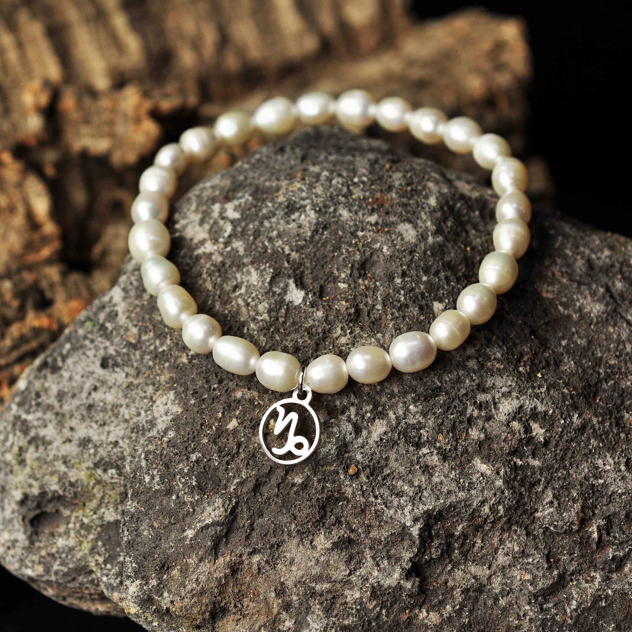 Wit zoetwater parel armband met zilver edelstalen symbool sterrenbeeld steenbok liggend op zwarte steen | Parel armband Zilveren Sterrenbeeld Steenbok