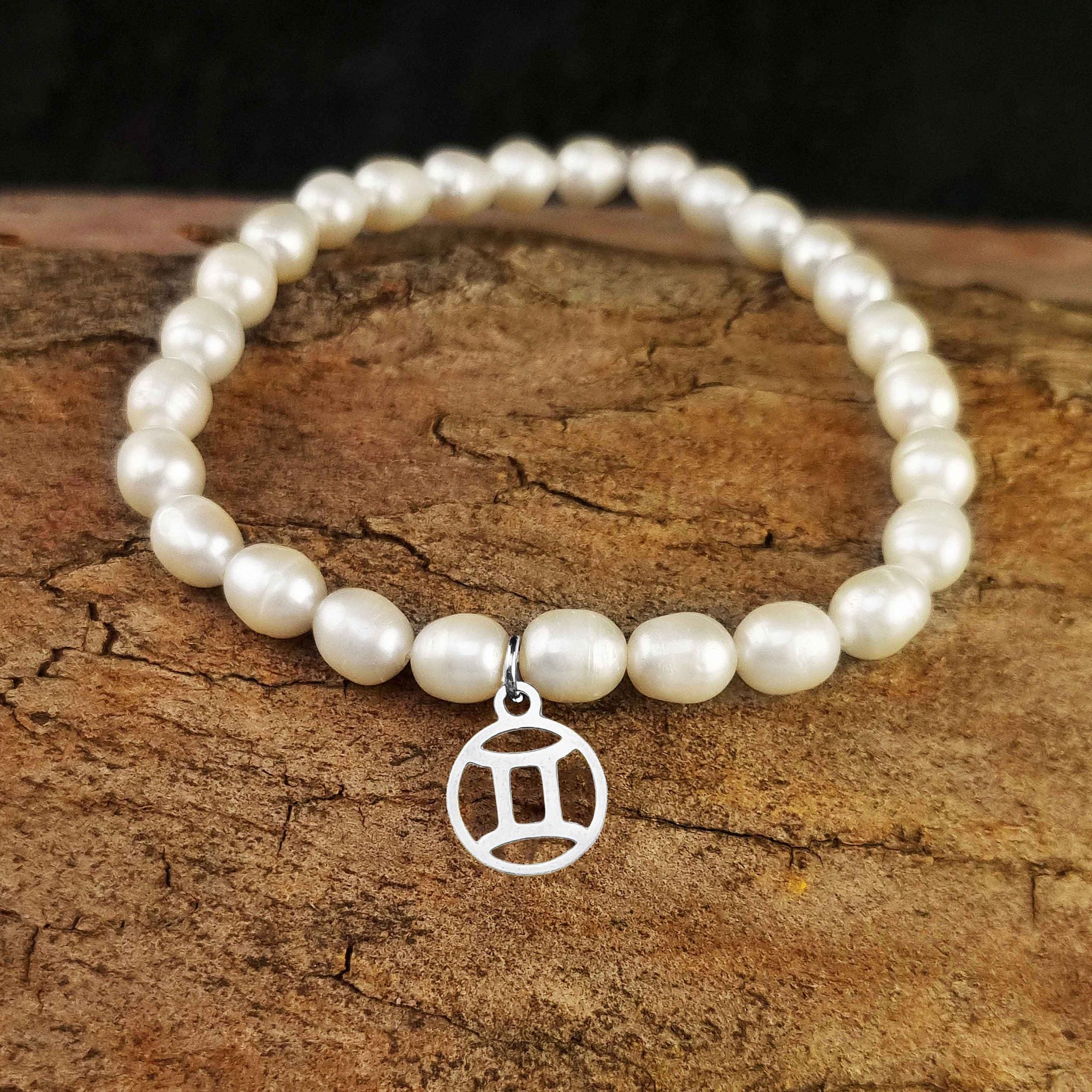 Wit zoetwater parel armband met zilver edelstalen symbool van sterrenbeeld Tweeling liggend op hout | Zilveren Sterrenbeeld Tweeling