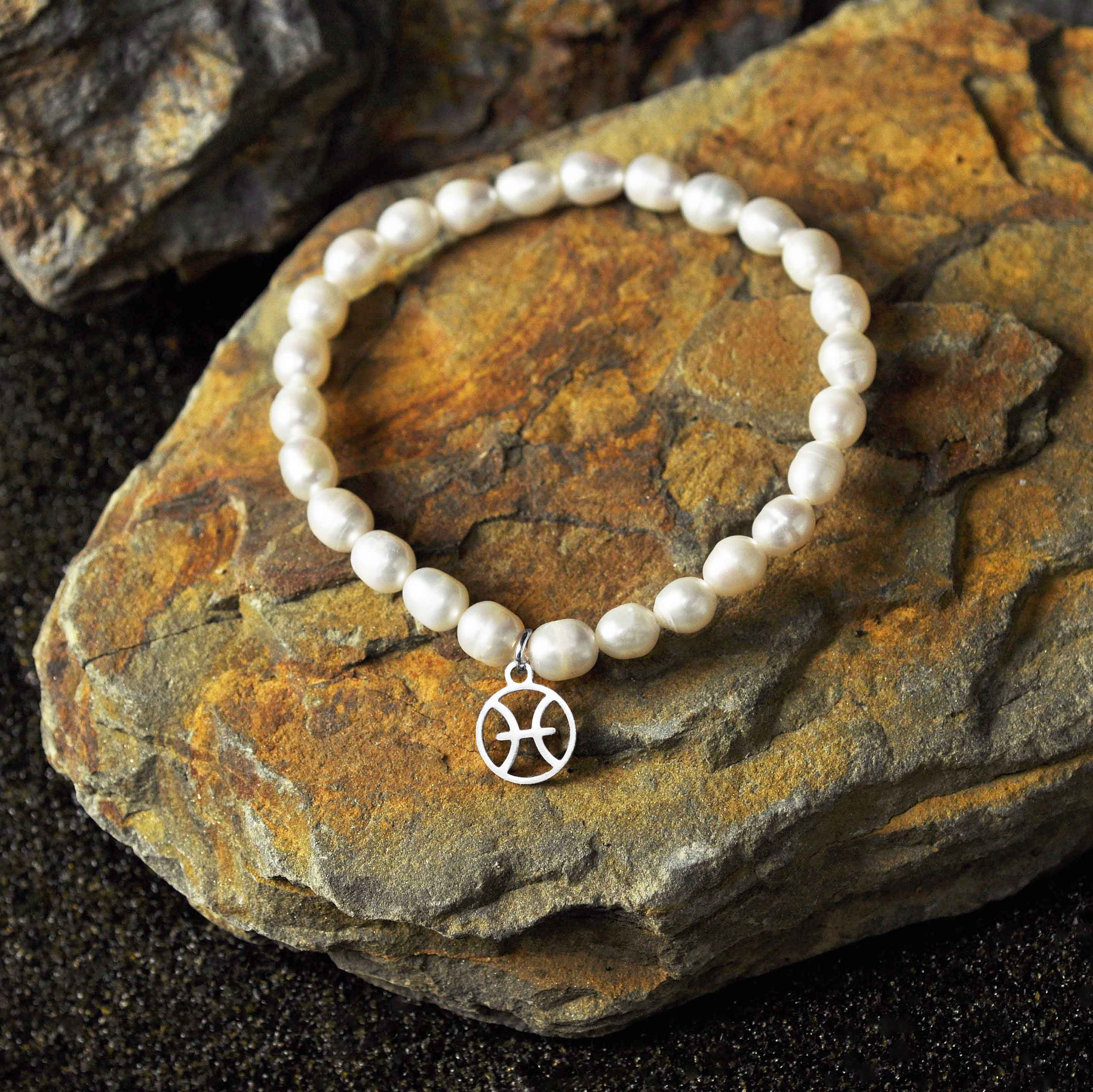 Wit zoetwater parel armband met zilver edelstalen symbool van sterrenbeeld Vissen liggend op steen | Parel armband Zilveren Sterrenbeeld Vissen