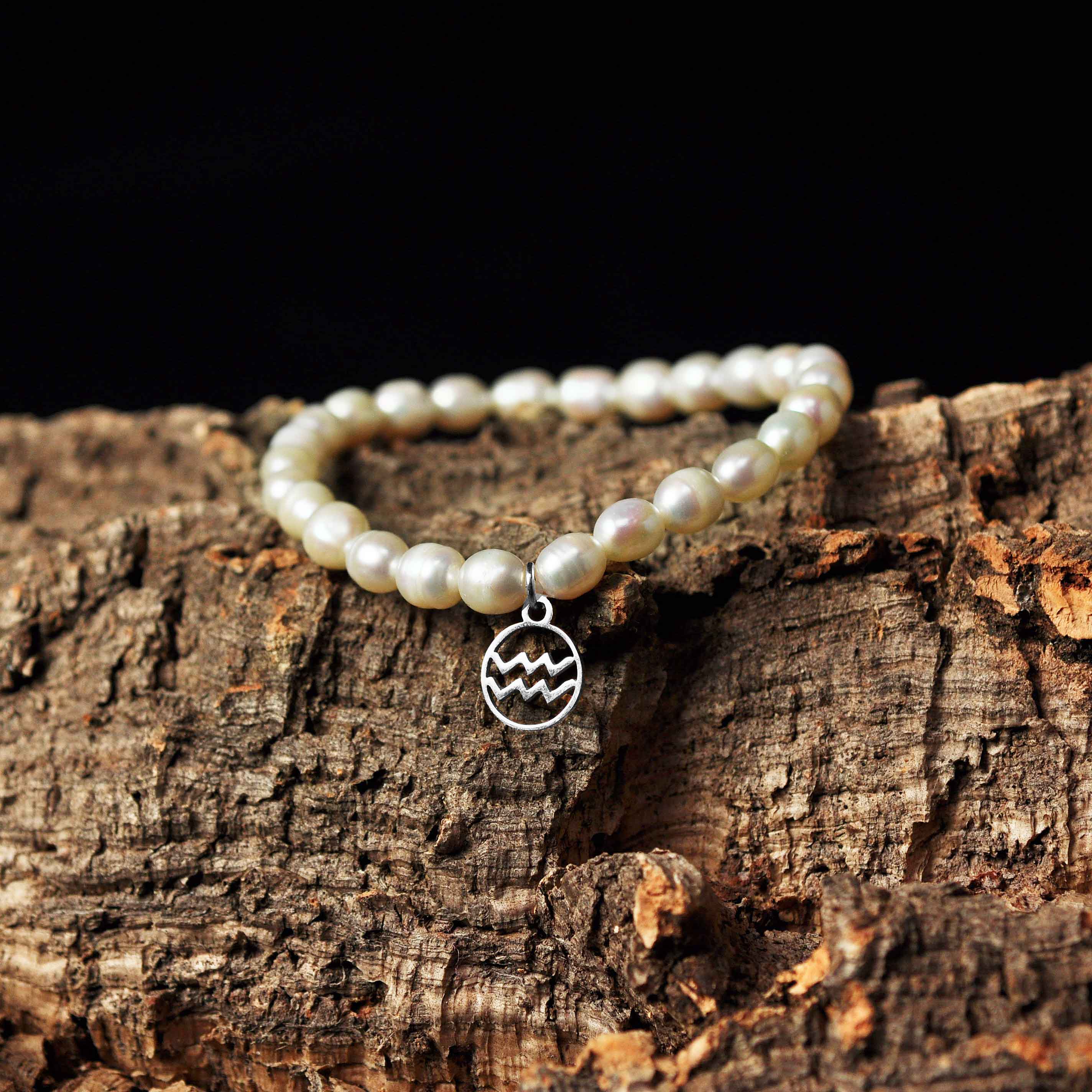 Wit zoetwater parel armband met zilver edelstalen symbool van sterrenbeeld Waterman liggend op schors | Parel armband Zilveren sterrenbeeld Waterman