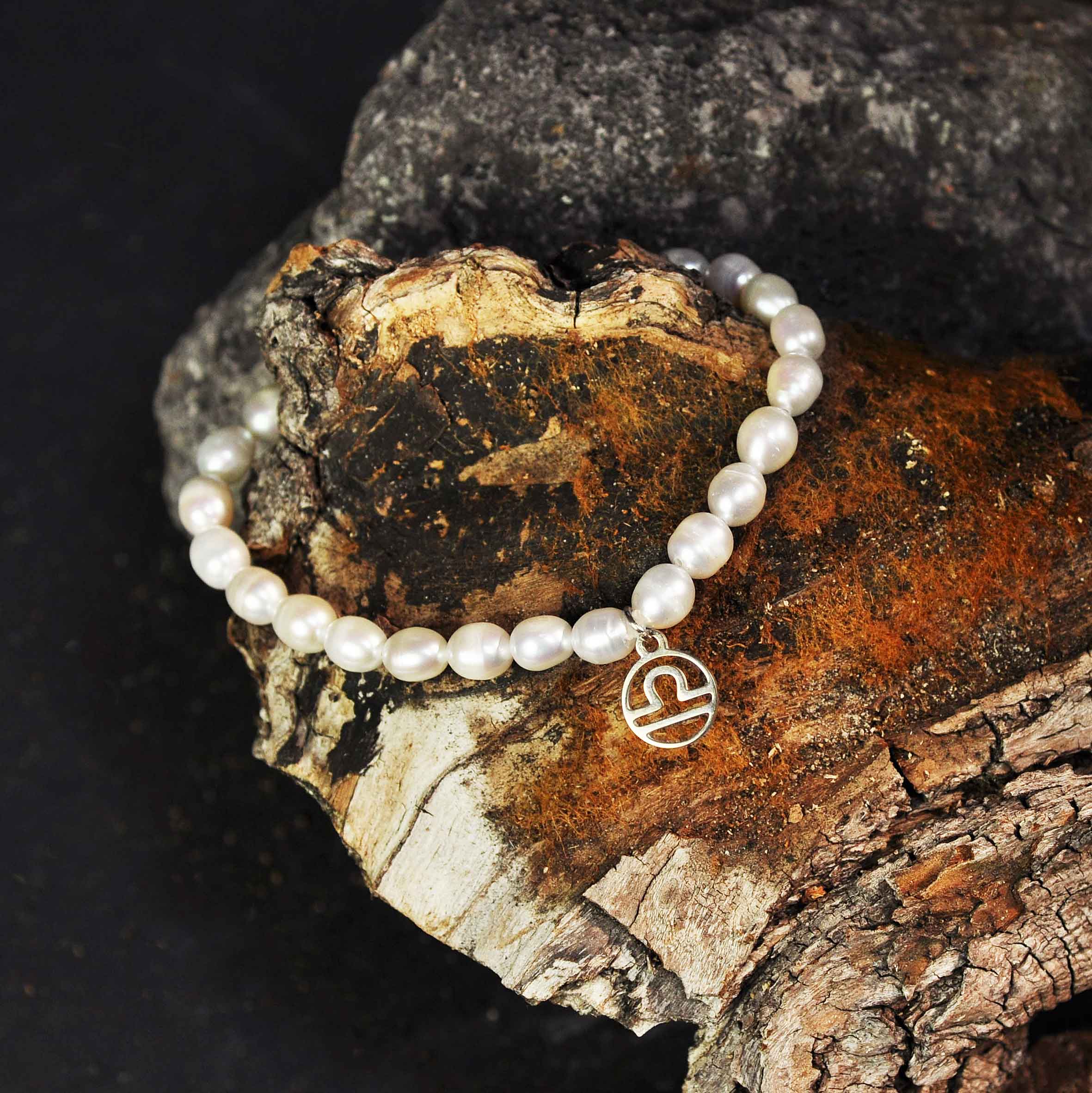 Wit zoetwater parel armband met zilver edelstalen symbool van sterrenbeeld Weegschaal liggend op hout | Armband Zilveren Sterrenbeeld Weegschaal