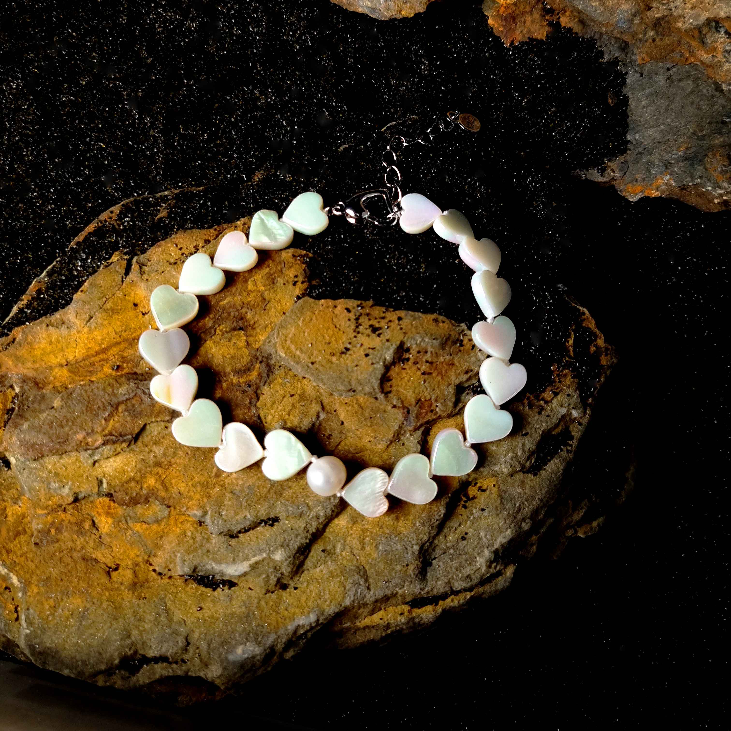 Wit zoetwater parel armband met wit parelmoeren hartjes liggend op zwart zand | White Pearl Heart Shell