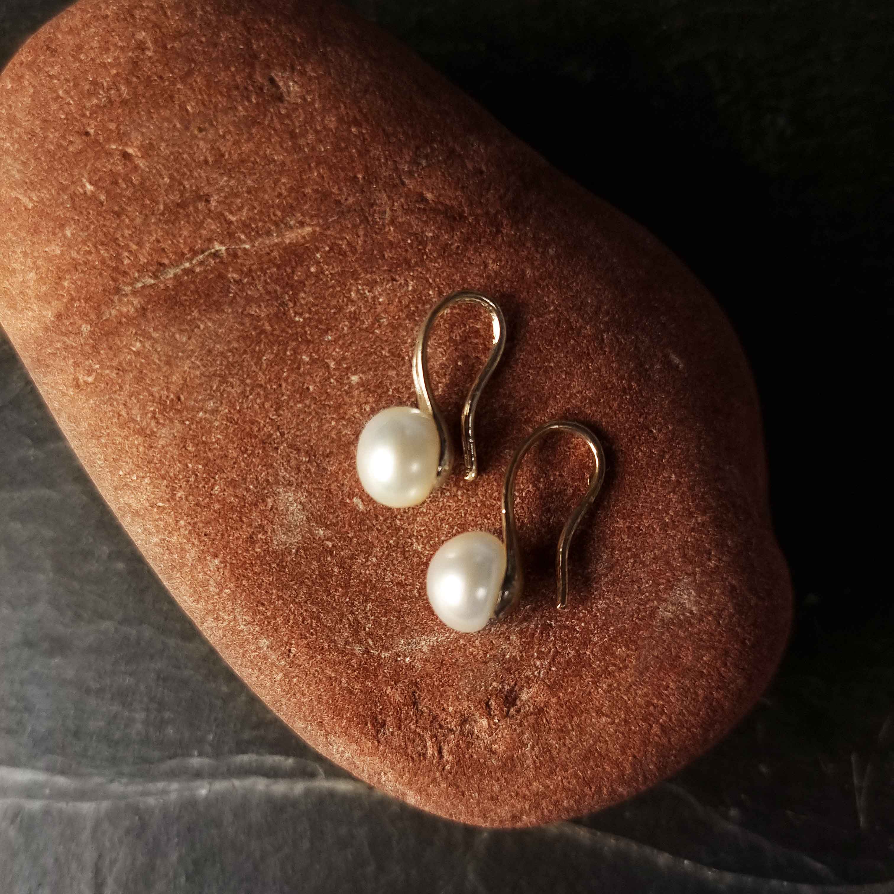 Witte zoetwater parel oorbellen liggend op rode steen | Leis White