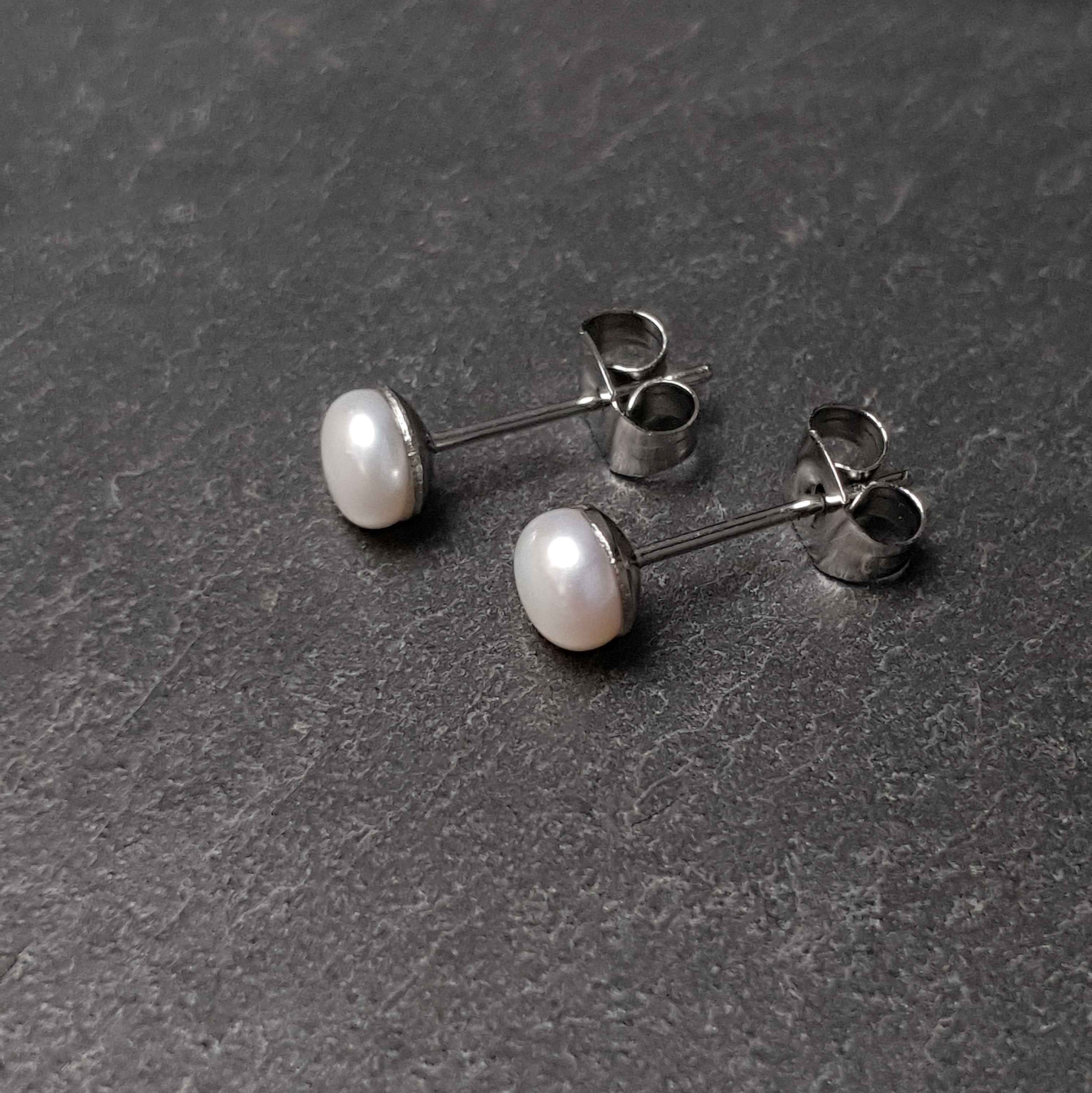 Witte zoetwater parel oorbellen met edelstaal liggend op leisteen | Little Pearl