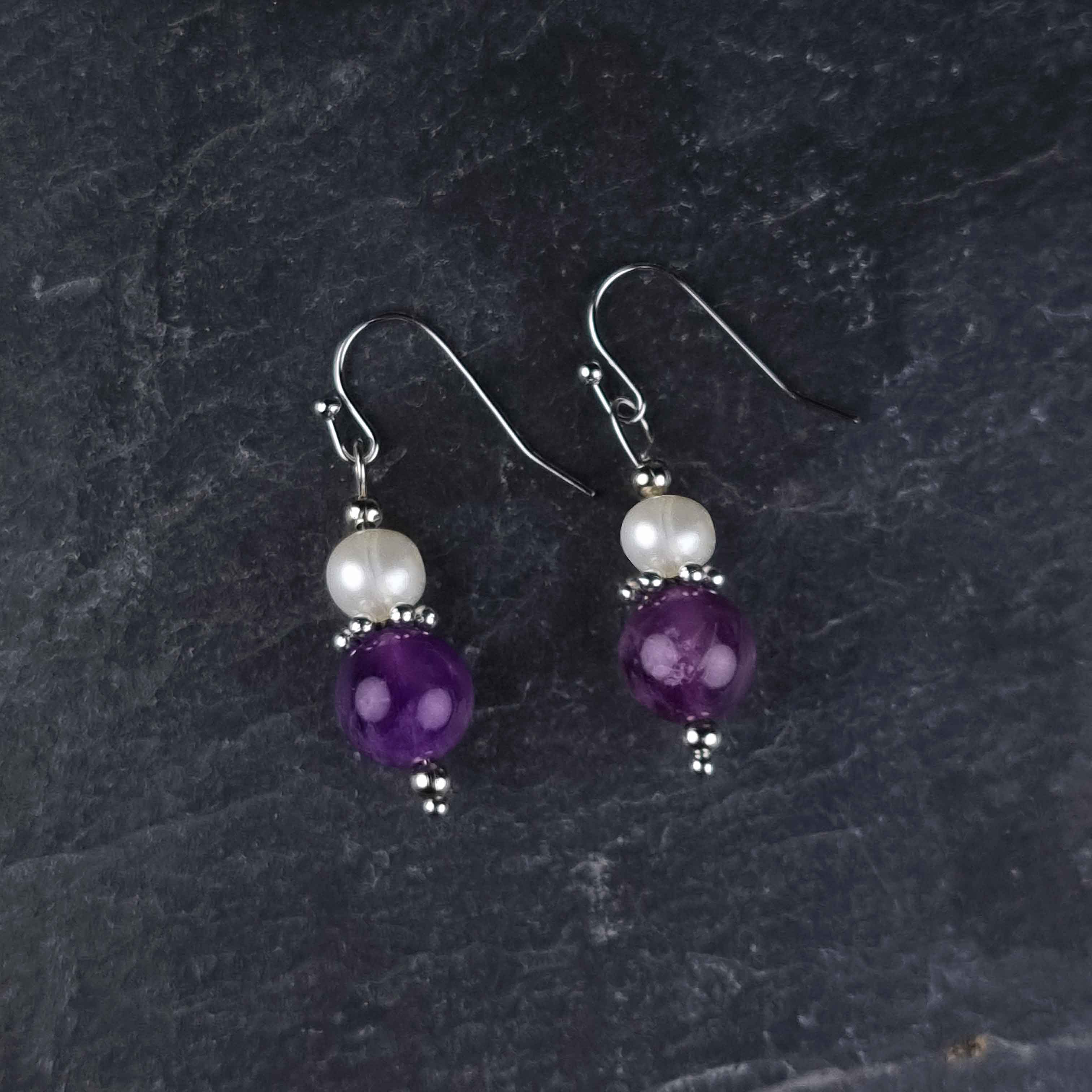 Witte zoetwater parel oorbellen met amethist en sterling zilver (925) liggend op leisteen | Amilia Amethyst