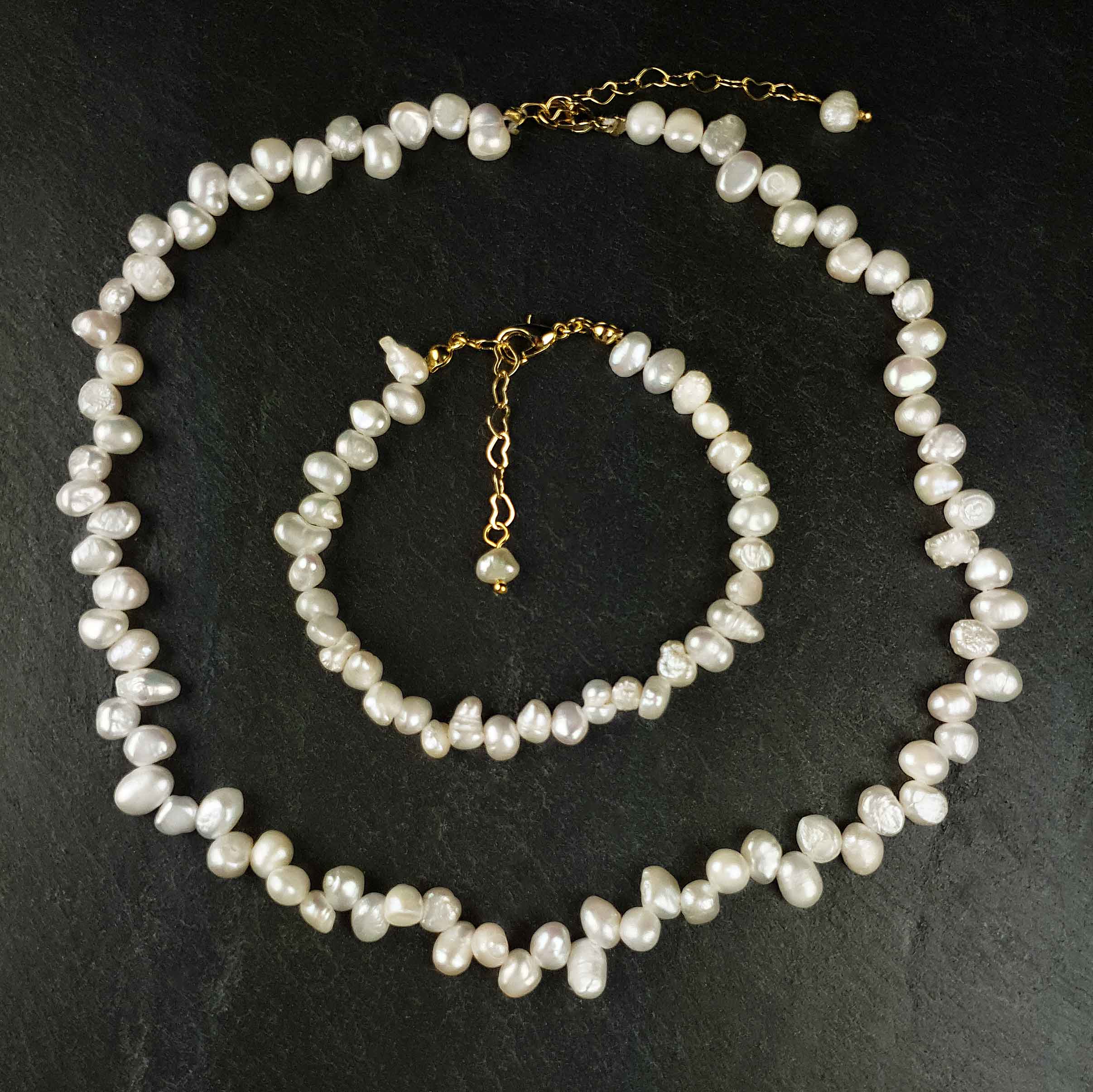Wit zoetwater parel set bestaande uit een witte zoetwater parelketting en parel armband met goud edelstalen slotje en verlengketting liggend op zwarte leisteen | set Adalyn
