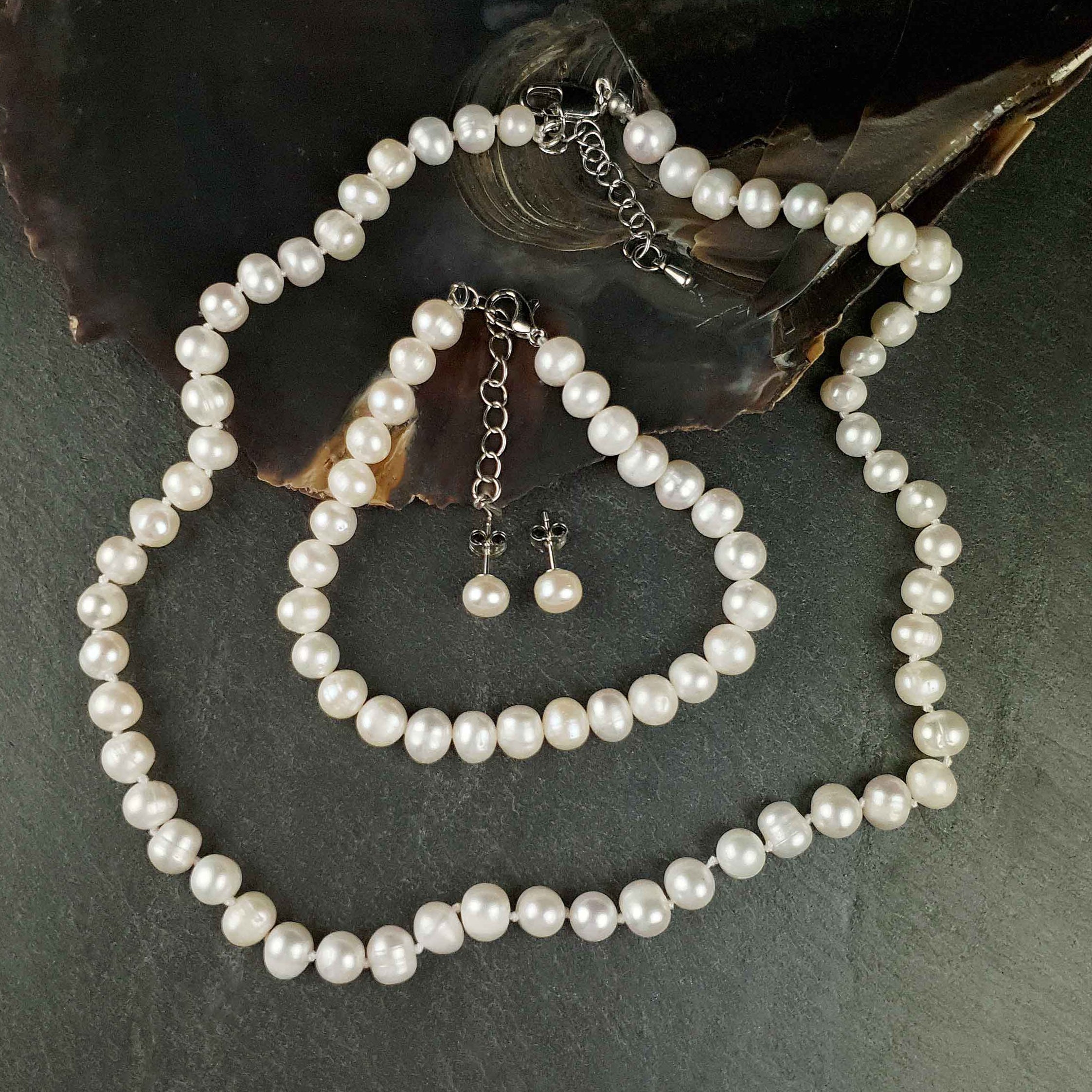 Handgeknoopte parel set bestaande uit een parelketting, parel armband en parel oorbellen met witte parels en sterling zilver (925) liggend op leisteen | set Bella
