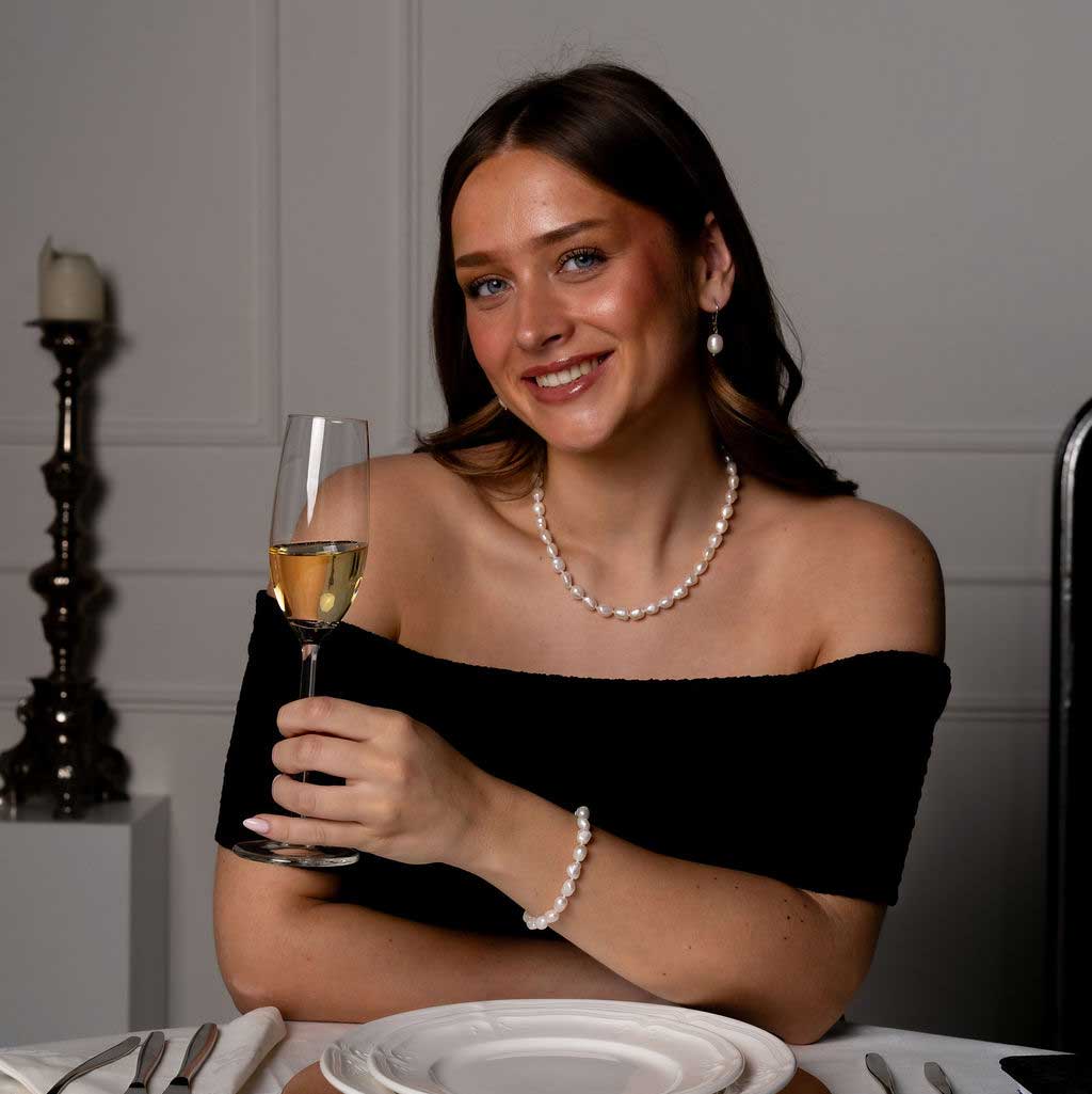 Handgeknoopte zoetwater parelketting, armband en oorbellen met witte parels op model aan tafel met glas | Wola
