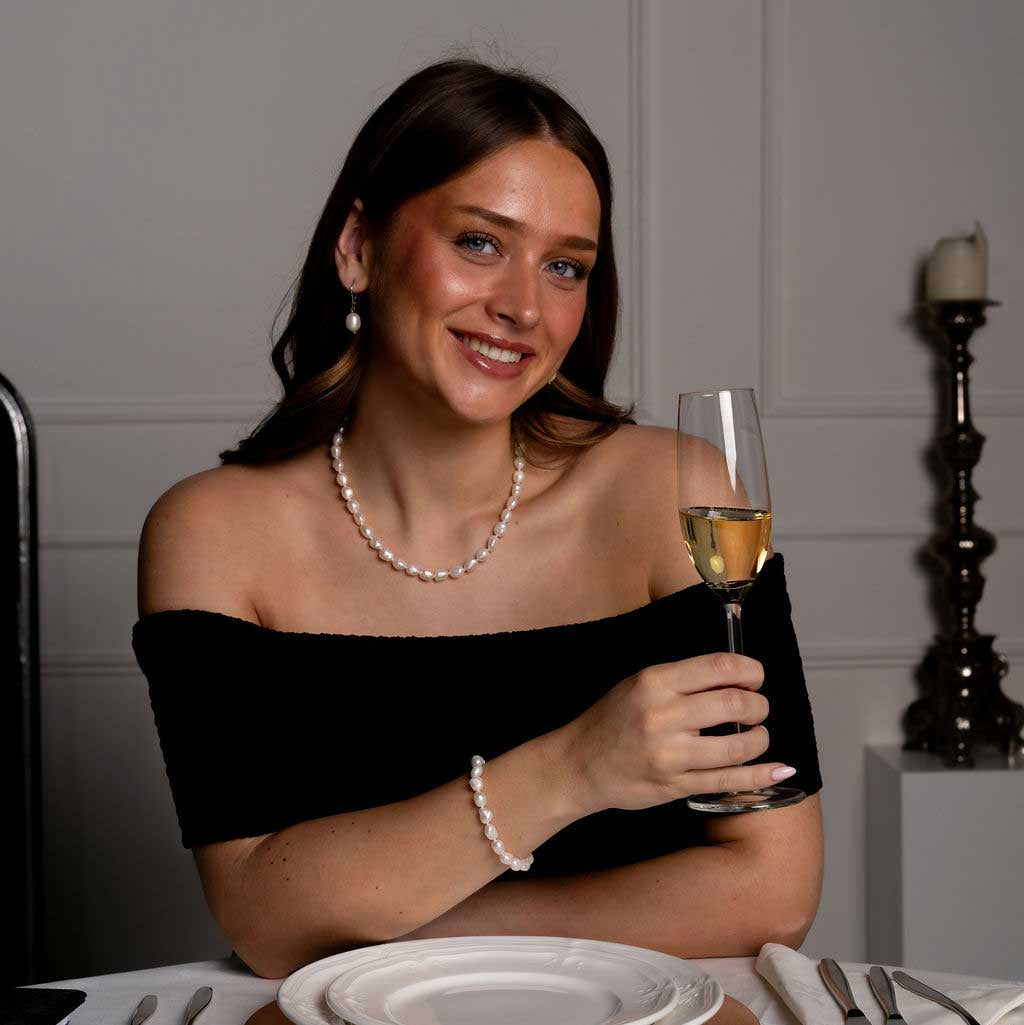 Handgeknoopte zoetwater parelketting, armband en oorbellen met witte parels op model aan tafel met glas | Wola