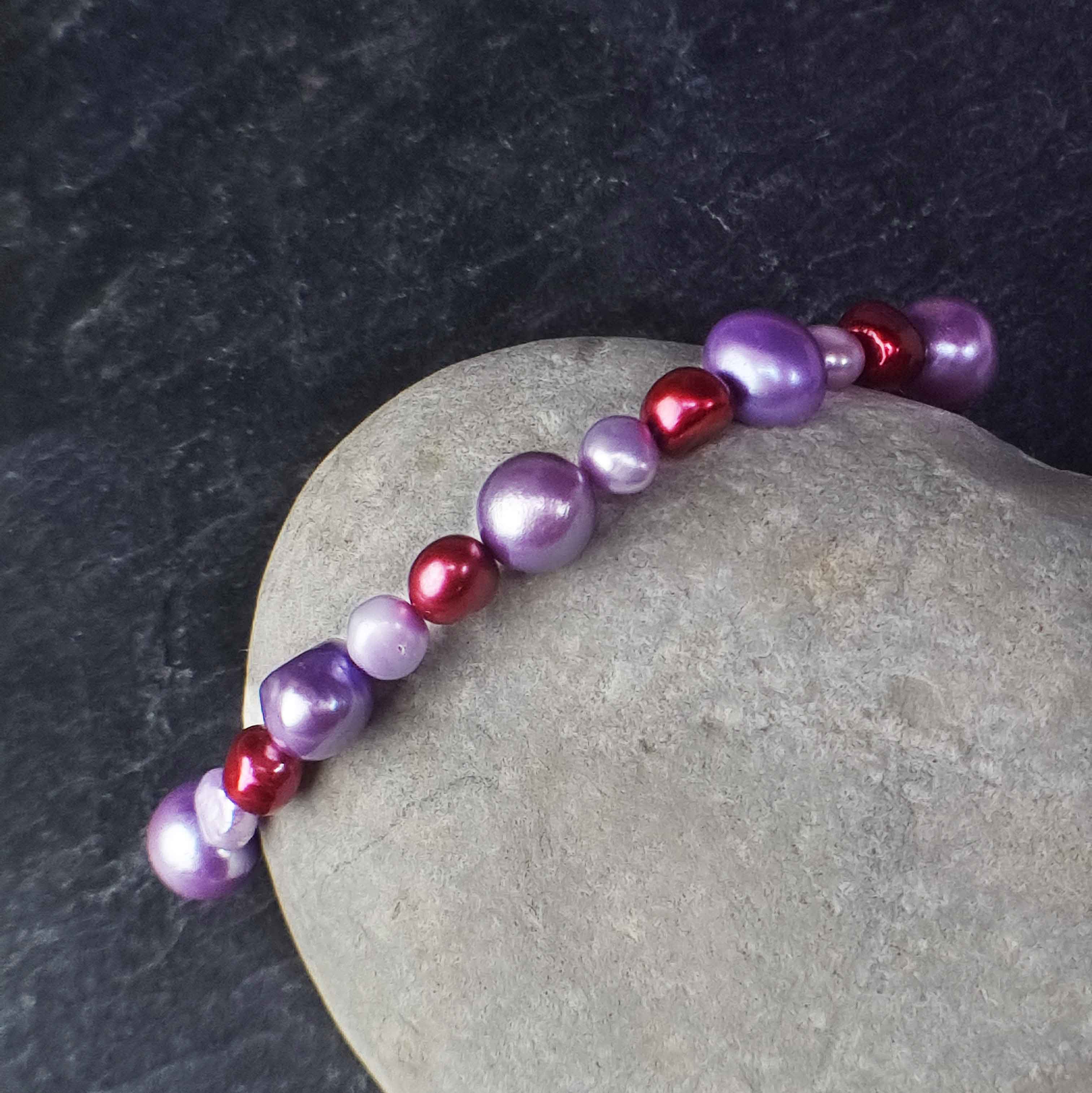Zoetwater parel armband met lila en rode parels liggend tegen witte steen | Pulla