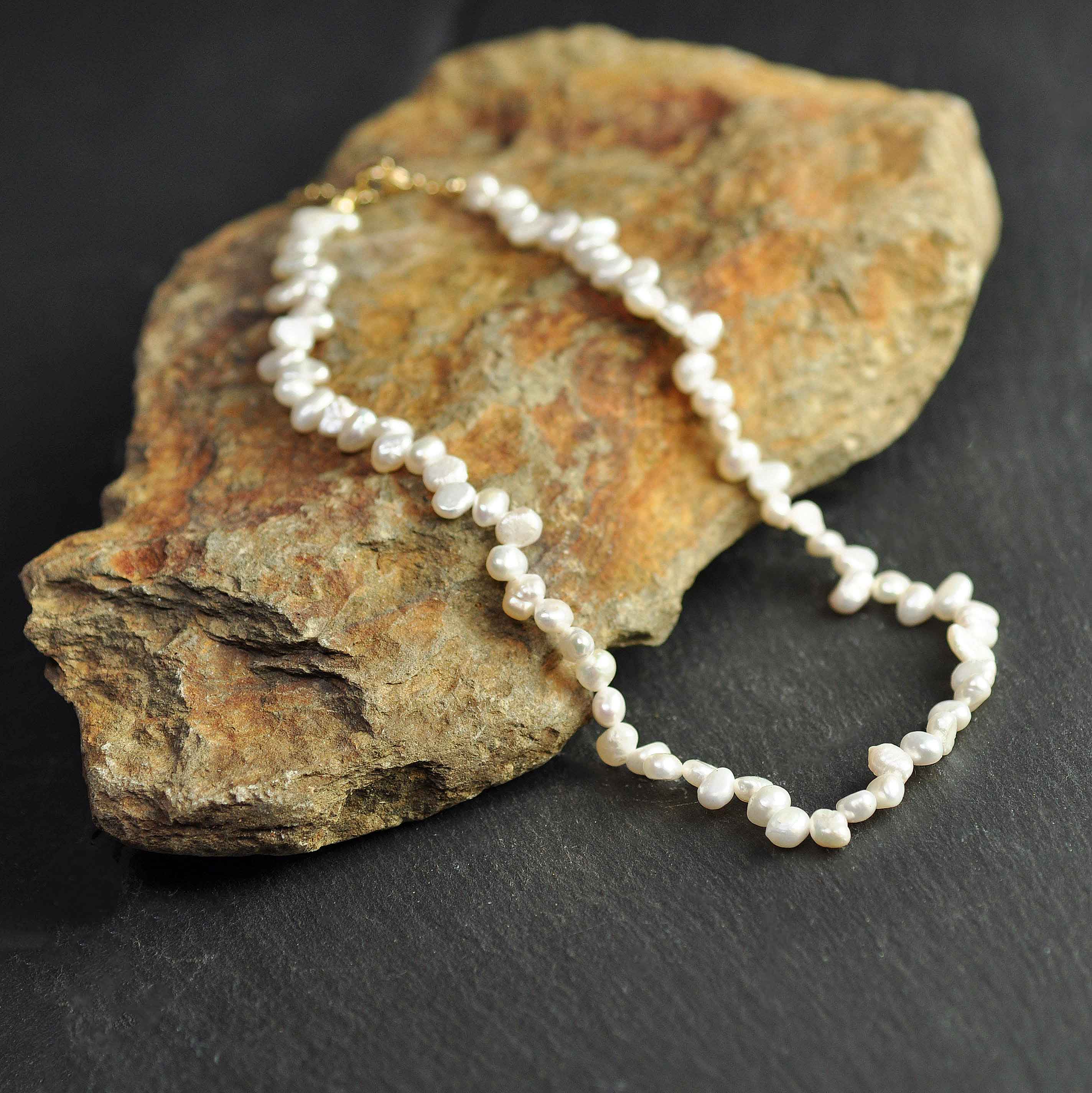 Wit zoetwater parelketting met goud edelstalen slotje en verlengketting liggend op oranje steen | Adalyn