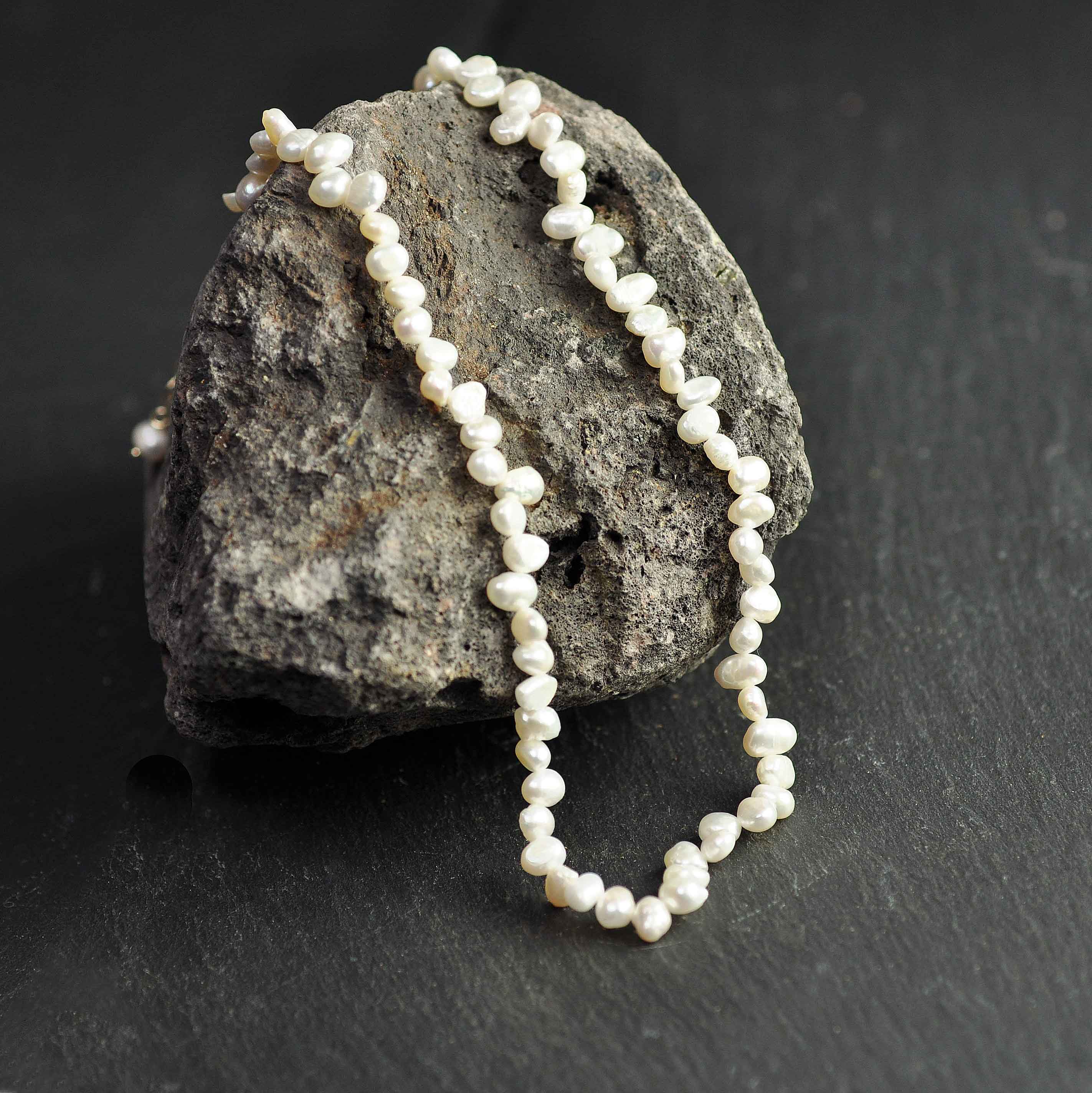 Wit zoetwater parelketting met goud edelstalen slotje en verlengketting liggend op rots | Adalyn