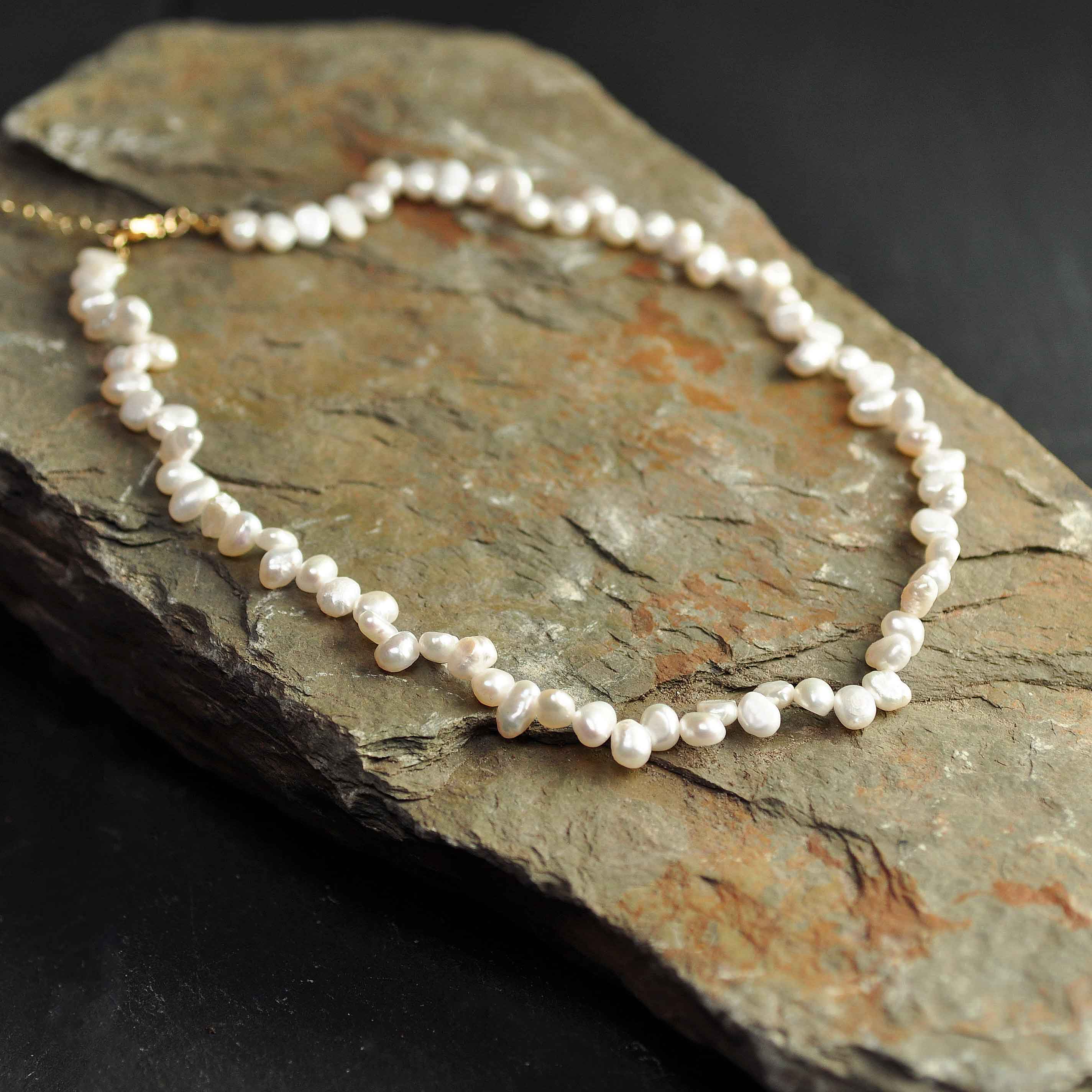 Wit zoetwater parelketting met goud edelstalen slotje en verlengketting liggend op steen | Adalyn