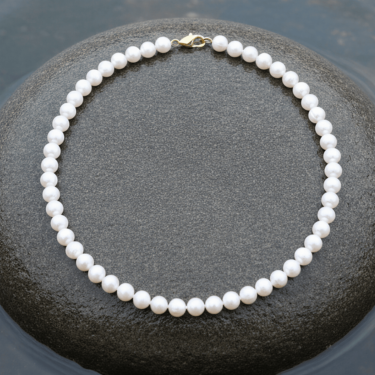 Witte zoetwater parelketting met goud edelstalen slotje liggend op steen in water | Bella Gold