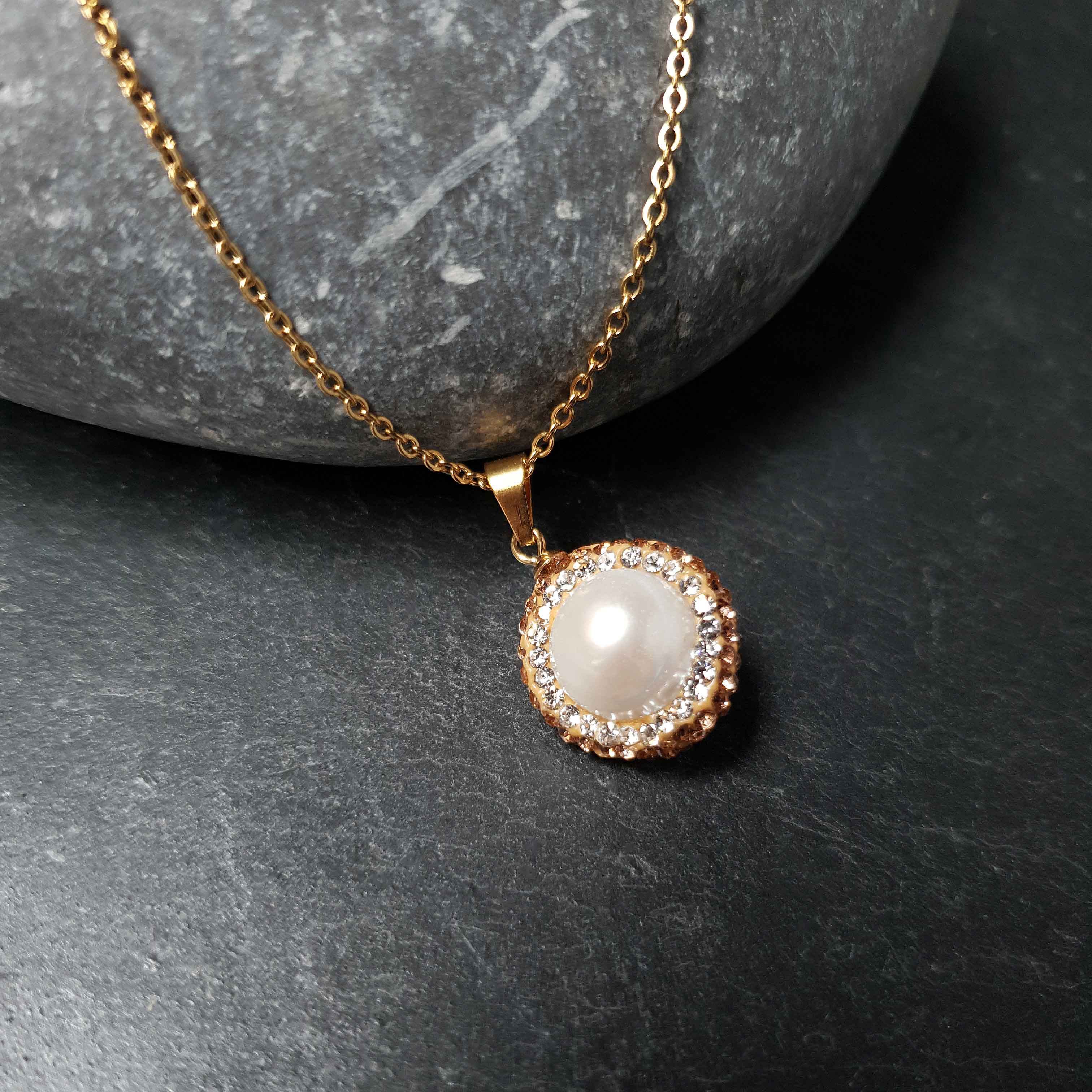 Detail van zoetwater parelketting met witte parel hanger, gouden stras steentjes en goud edelstaal liggend op steen | Bright Golden Pearl