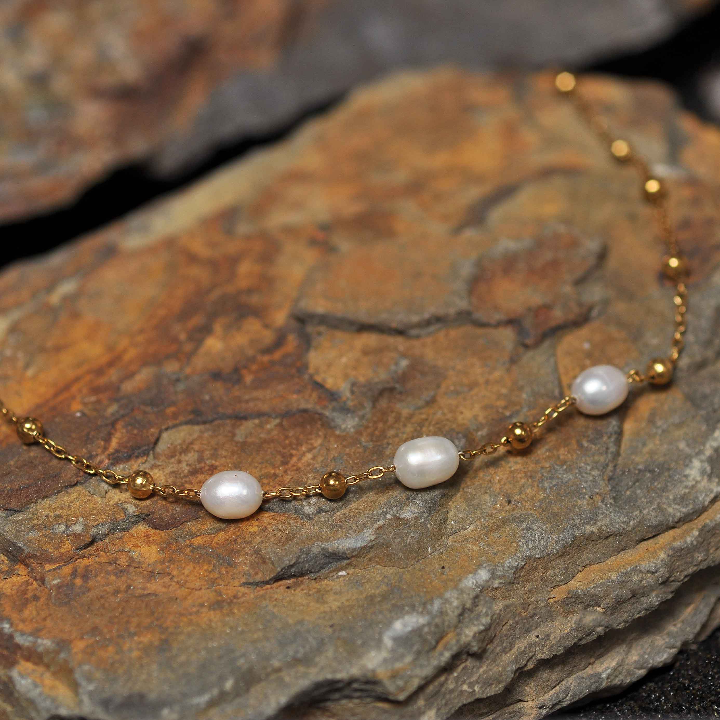 Witte zoetwater parelketting met goud edelstaal liggend op oranje steen | Parelketting Eline Goud