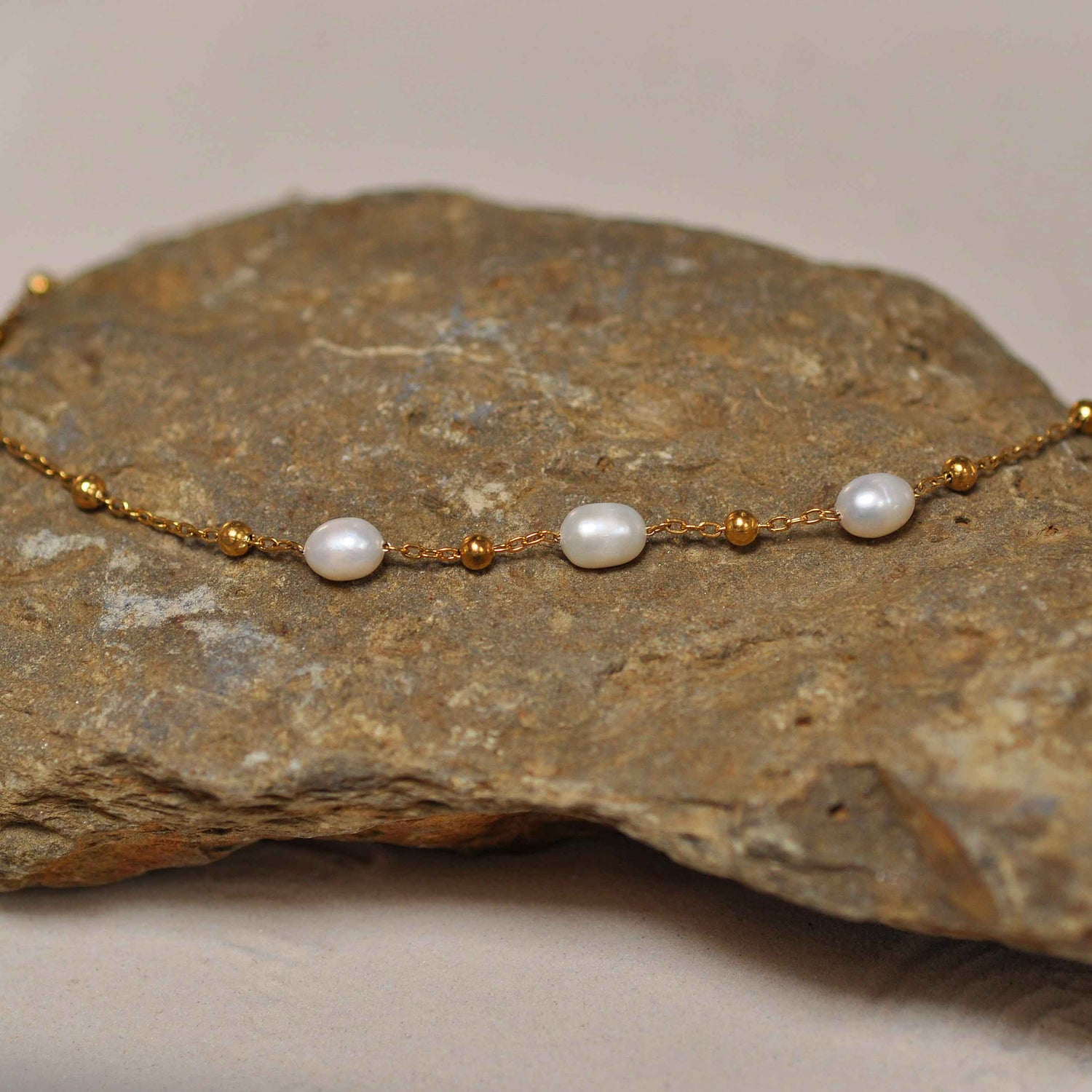 Witte zoetwater parelketting met goud edelstaal liggend op steen | Parelketting Eline Goud