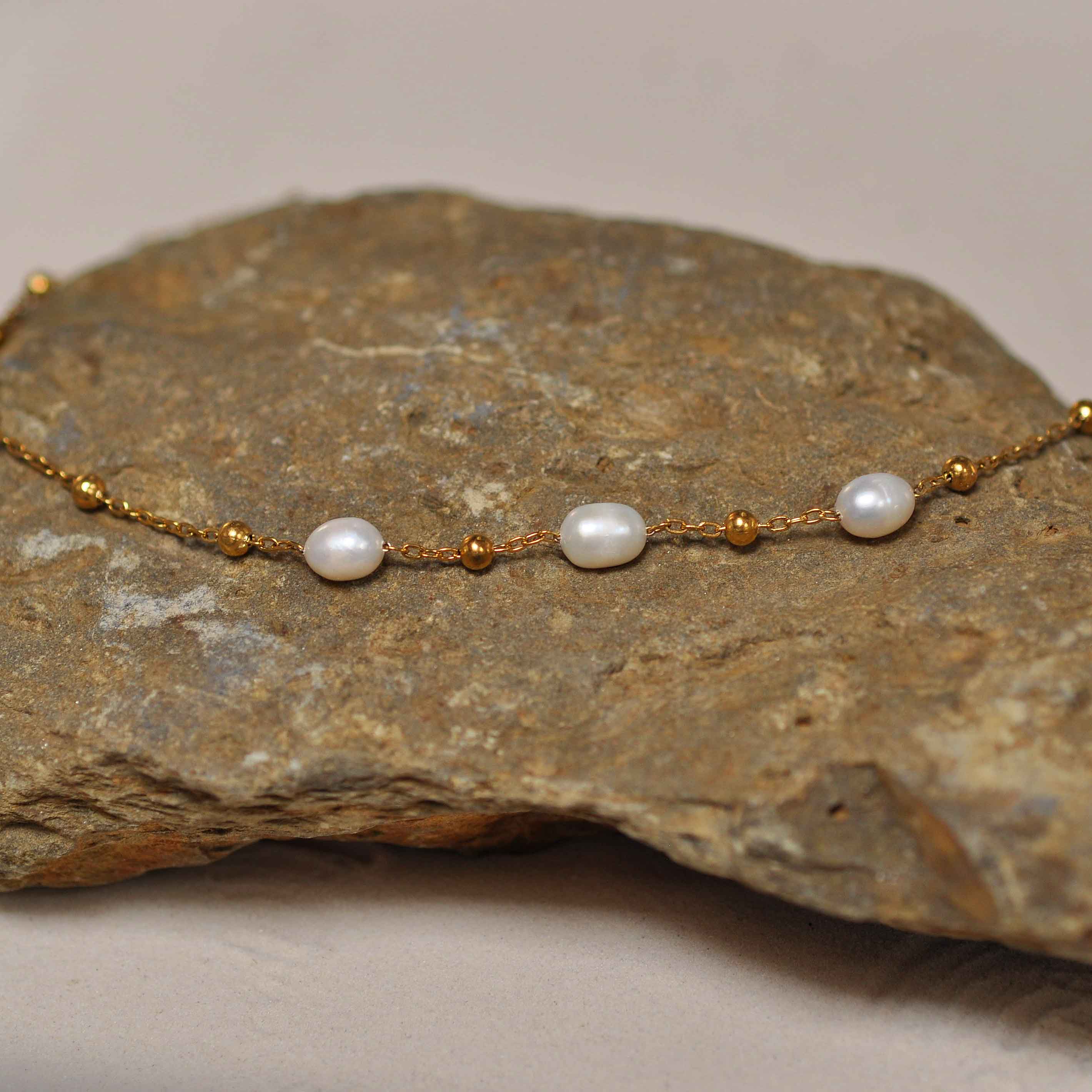 Witte zoetwater parelketting met goud edelstaal liggend op steen | Parelketting Eline Goud