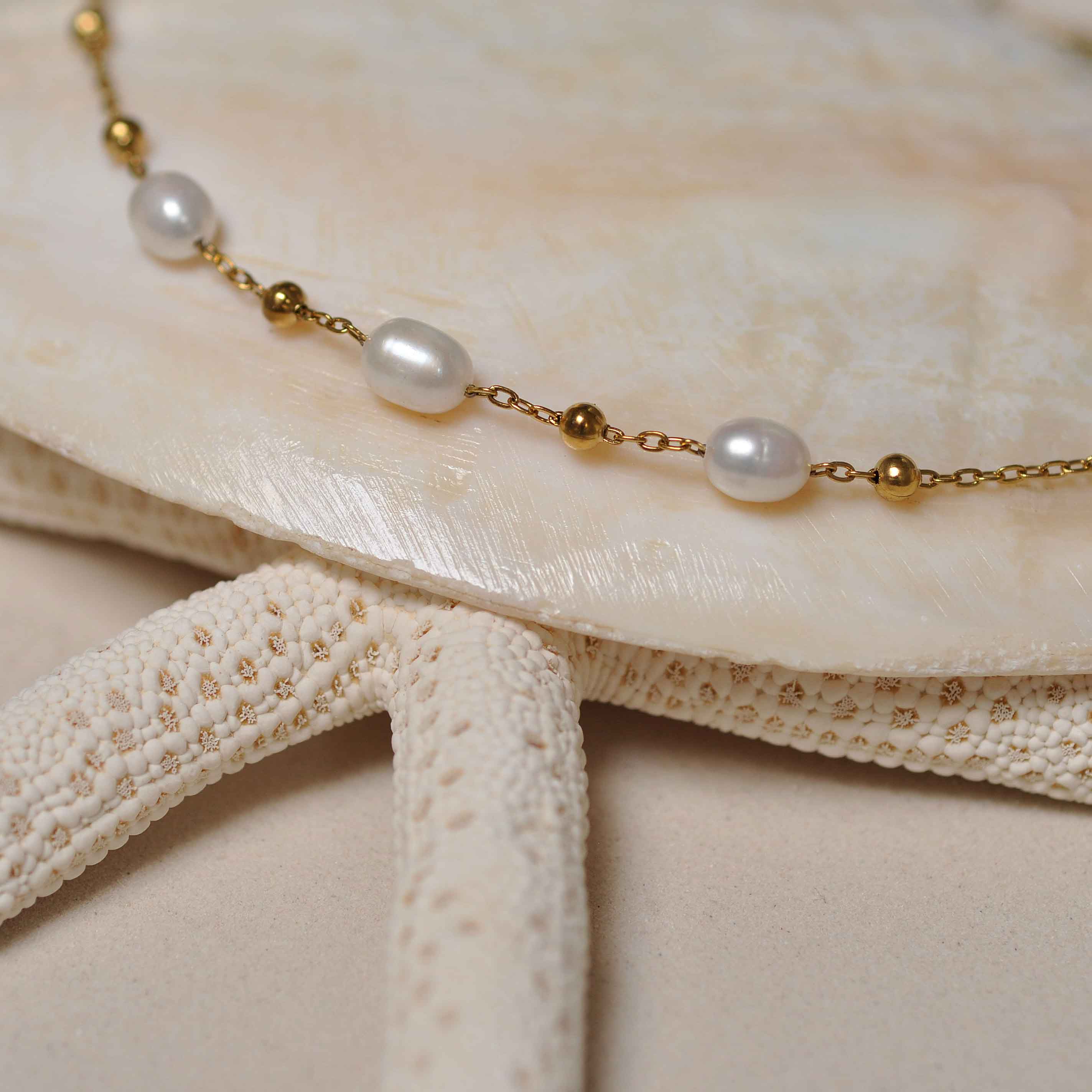 Witte zoetwater parelketting met goud edelstaal liggend op witte schelp | Parelketting Eline Goud