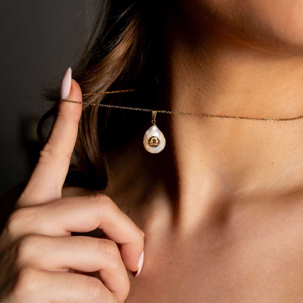 Detail van zoetwater parelketting met witte parel hanger met gouden symbool van sterrenbeeld weegschaal en goud edelstaal op model detail | Gouden Sterrenbeeld Weegschaal