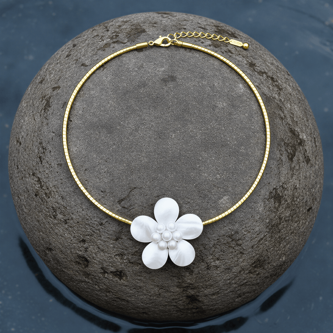 zoetwater parelketting met witte parels, wit parelmoer in de vorm van een bloem en goud edelstaal liggend op steen| Fleury W Gold