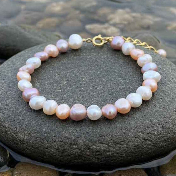 Zoetwater parel armband met witte, roze en zalm kleurige parels met goud edelstaal liggend op steen in water | Aza