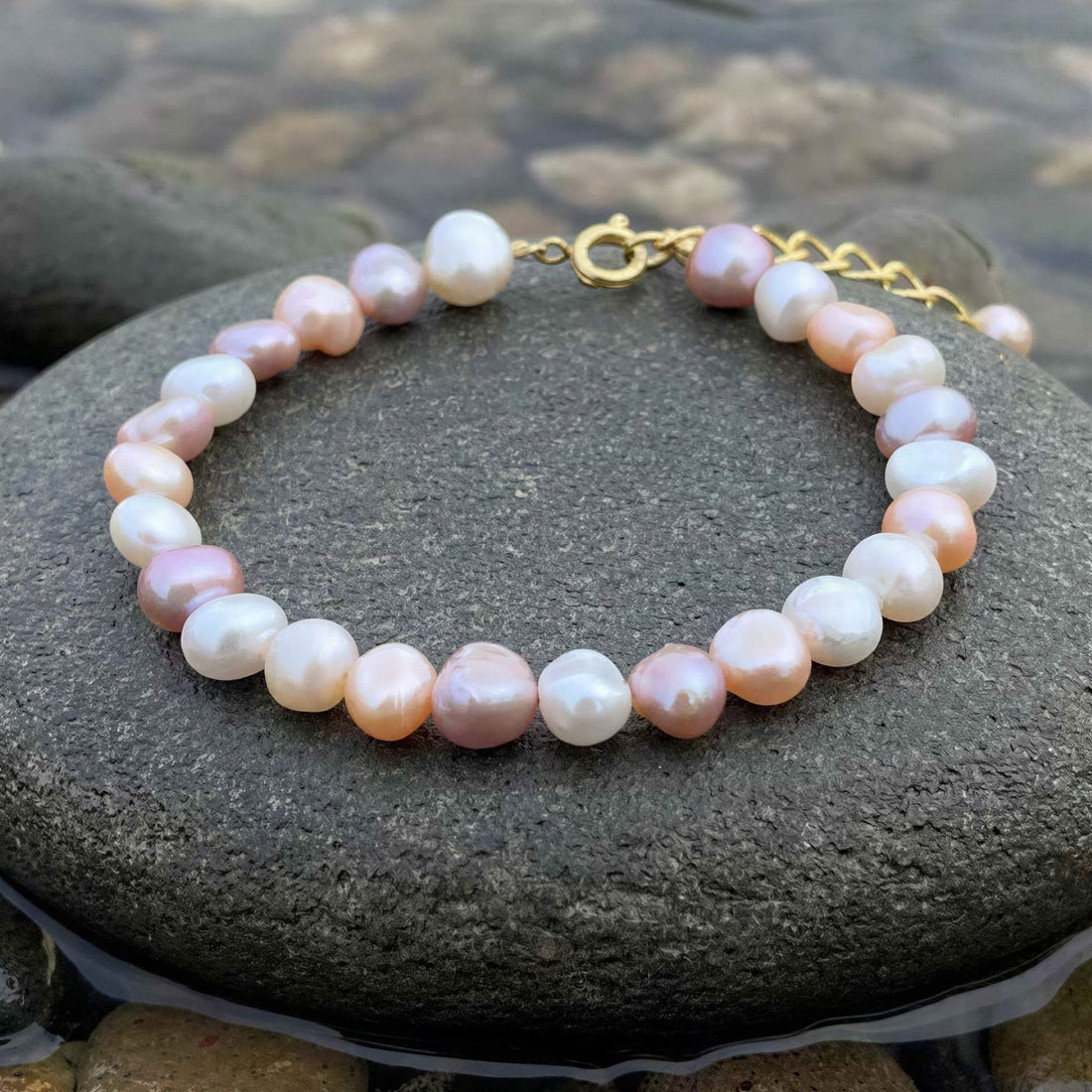 Zoetwater parel armband met witte, roze en zalm kleurige parels met goud edelstaal liggend op steen in water | Aza