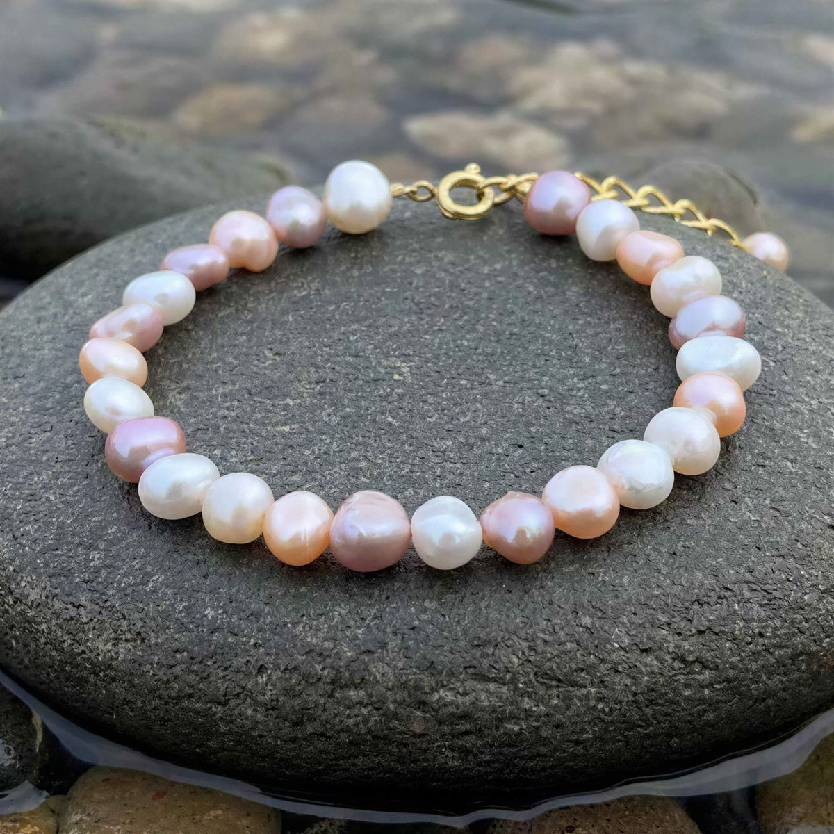 Zoetwater parel armband met witte, roze en zalm kleurige parels met goud edelstaal liggend op steen in water | Aza