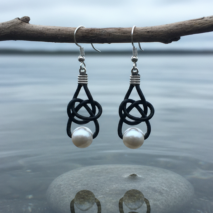Witte zoetwater parel oorbellen met zwart leer en sterling zilver (925) hangend boven water | Black Leather Pearl White