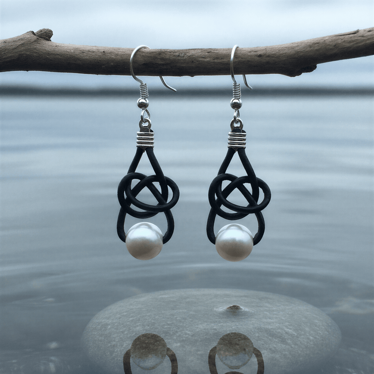 Witte zoetwater parel oorbellen met zwart leer en sterling zilver (925) hangend boven water | Black Leather Pearl White