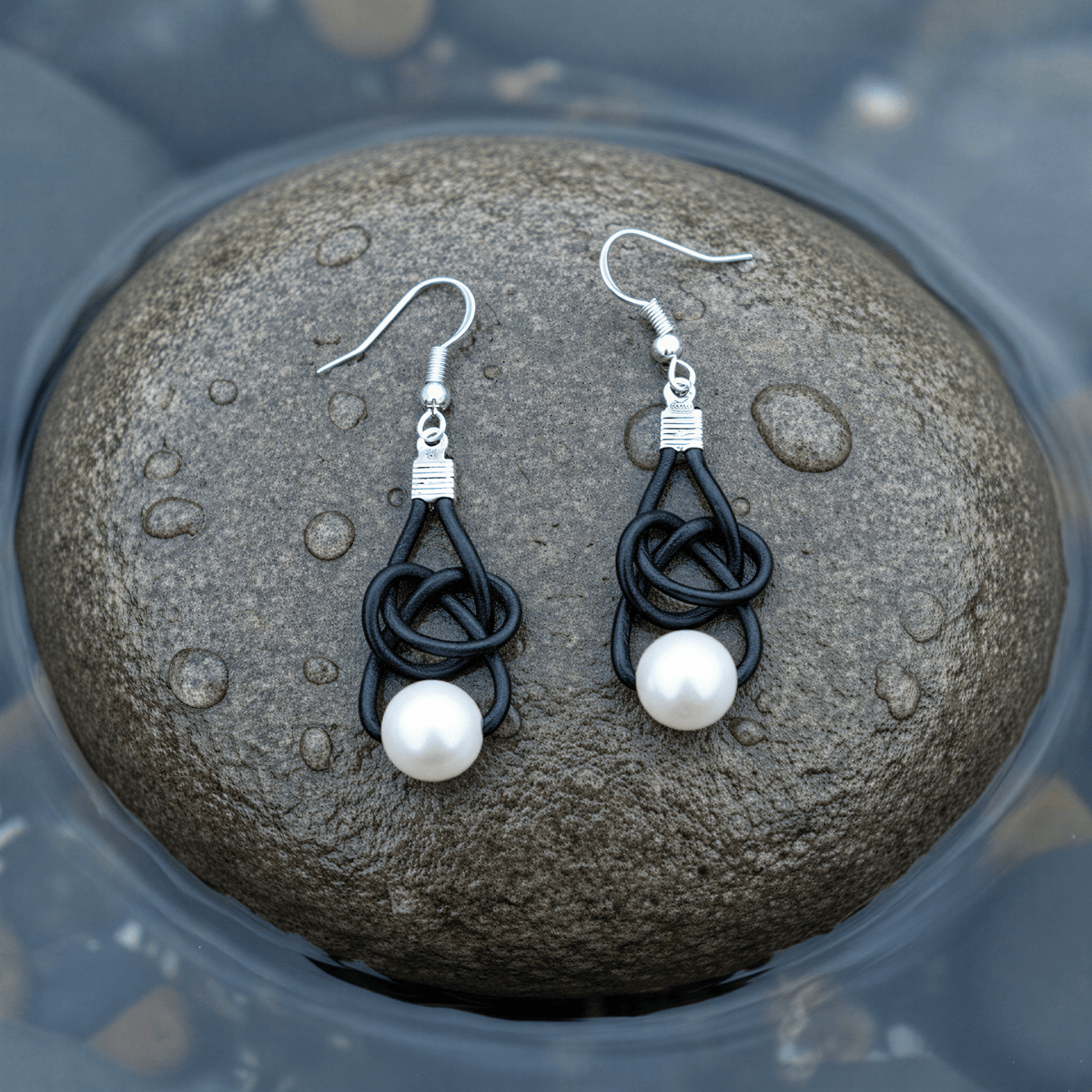 Witte zoetwater parel oorbellen met zwart leer en sterling zilver (925) liggend op natte steen | Black Leather Pearl White
