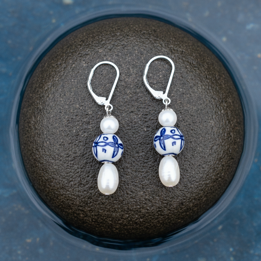 Zoetwater parel oorbellen met witte parels, parelmoer, Delfts blauwe ornament en edelstaal liggend op steen in water | Hollands Glorie Bedeltje
