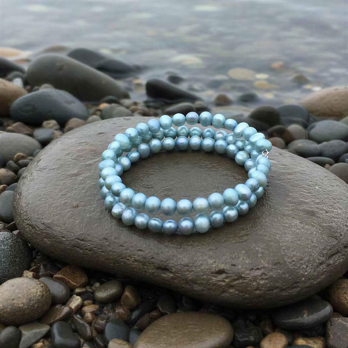 Zoetwater parel wikkel armband met aqua blauwe parels liggend op steen bij water | Zen Aqu