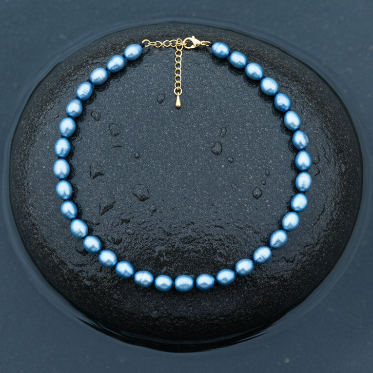 Blauw zoetwaterparel ketting met goud edelstalen slotje is volledig handgeknoopt met barok parels en ligt op steen in water | Blair