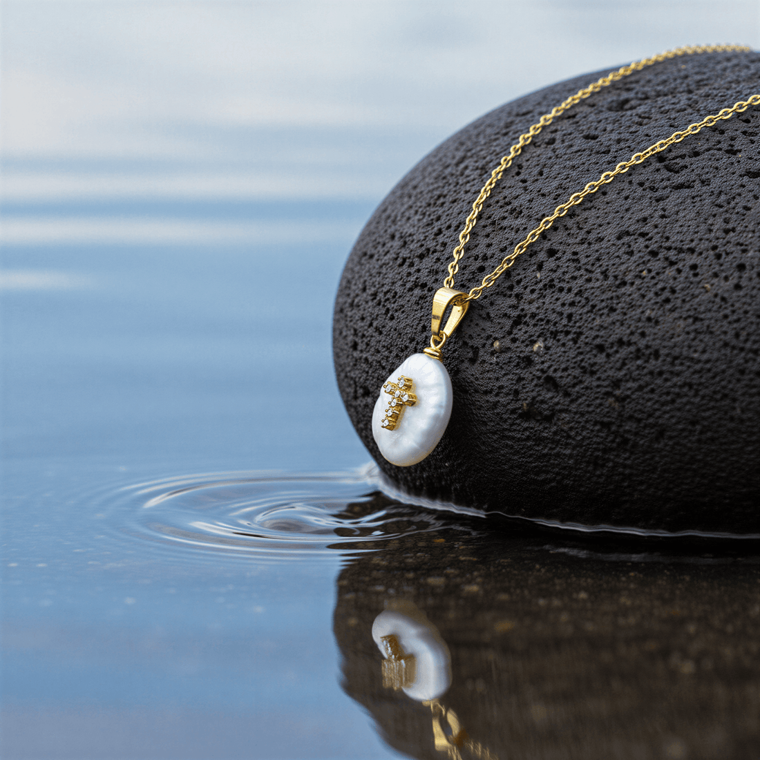 Detail van zoetwater parelketting met witte parel hanger met stras steentjes in kruis motief en goud edelstaal liggend op steen | Coin Pearl Golden Cross
