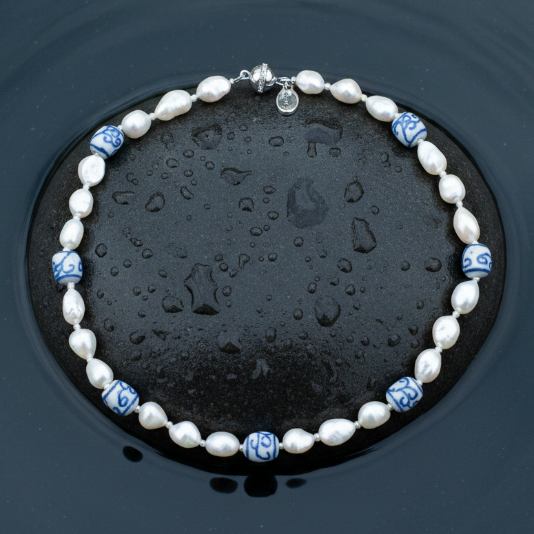 Zoetwater parelketting met witte parels, kralen met Delfts blauw motief en magneetslotje liggend op steen in water | Hollands Glorie Spiral White