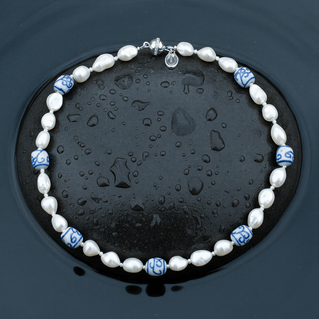 Zoetwater parelketting met witte parels, kralen met Delfts blauw motief en magneetslotje liggend op steen in water | Hollands Glorie Spiral White