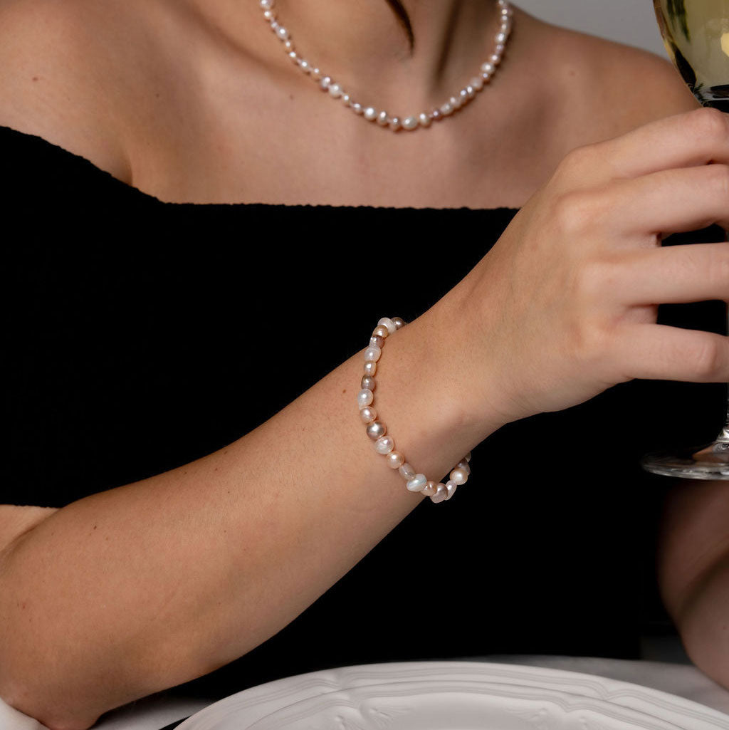 Elastisch zoetwater parel armband met witte, zalm en roze parels op model aan tafel | Pearl Soft Colors Pearl Small