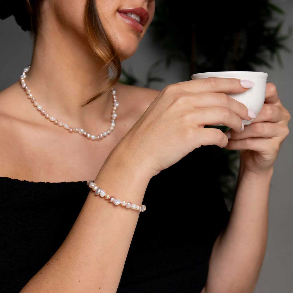 Elastisch zoetwater parel armband met witte, zalm en roze parels op model die thee drink | Pearl Soft Colors Pearl Small