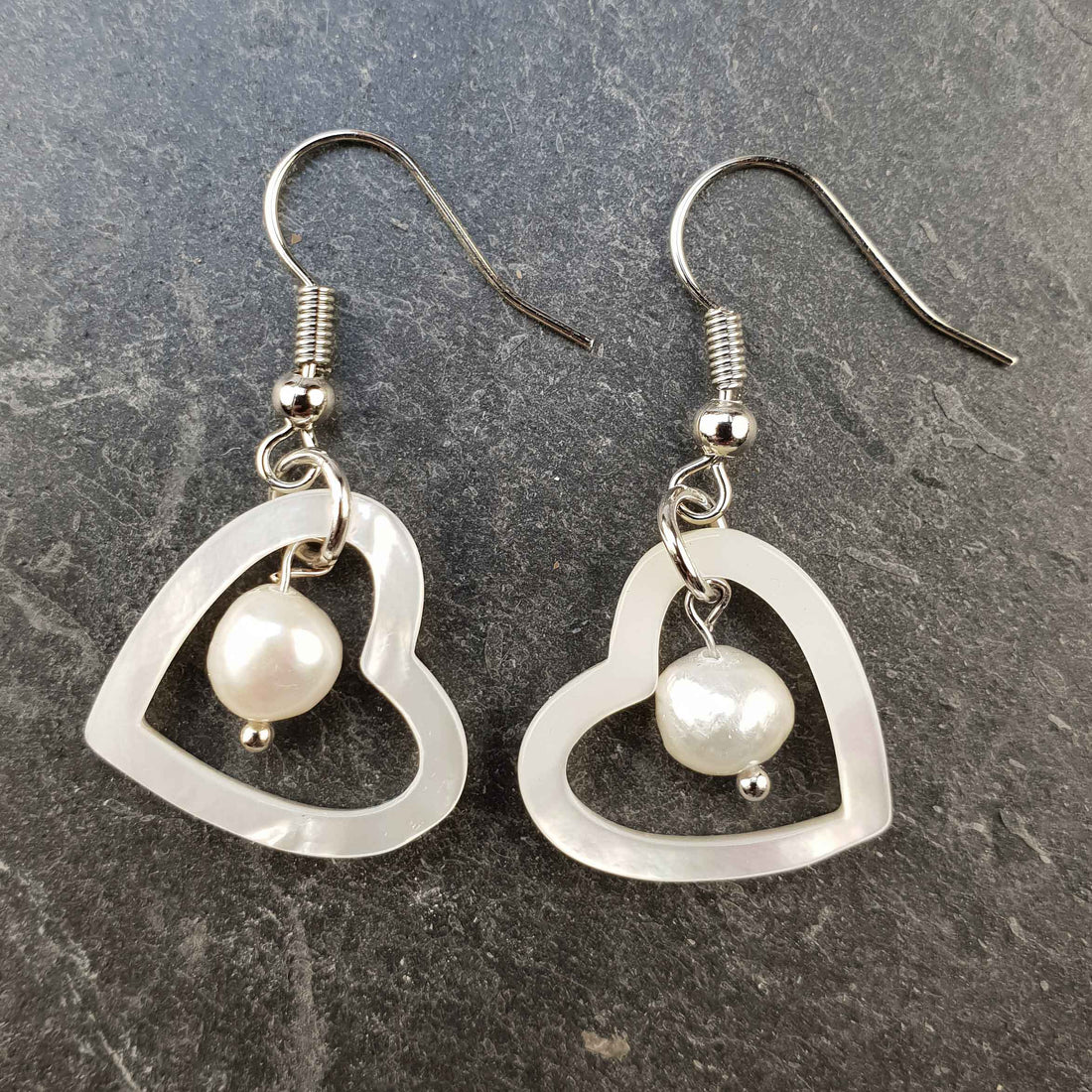 Witte zoetwater parel oorbellen met witte parel en parelmoer hart en sterling zilver (925) liggend op steen | Pearl Heart Shell