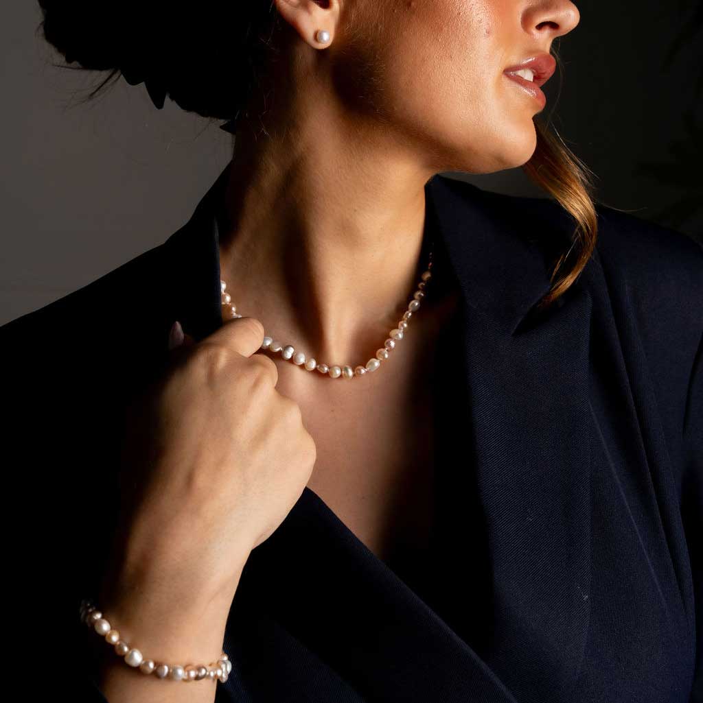 Handgeknoopte zoetwater parel set bestaande uit parelketting en parel armband met witte, zalm en roze parels en sterling zilver (925) op model met colbertje detail | set Pearl Colors Small