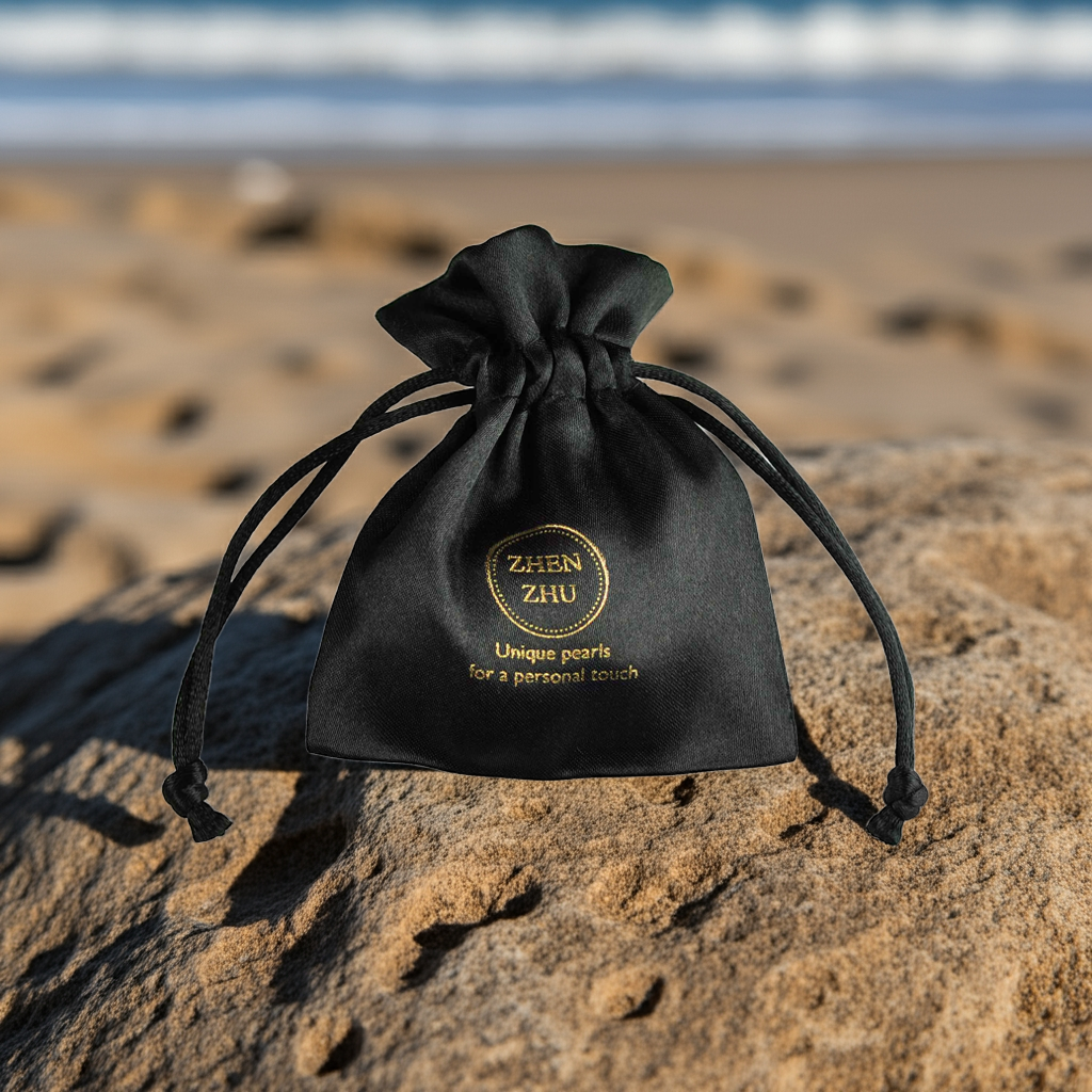 Zwart satijnen sieraden zakje met gouden logo Zhen Zhu op rots bij de zee