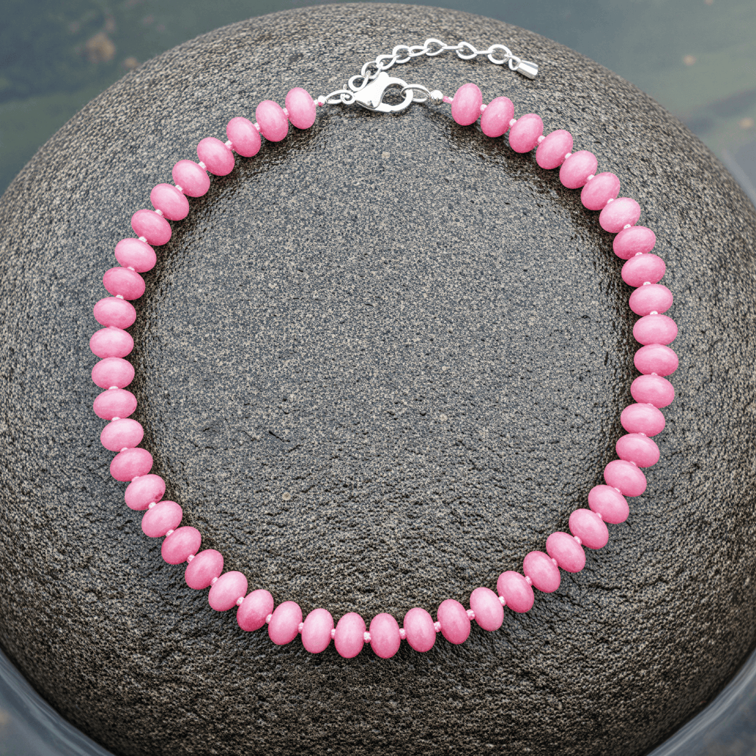 Donker roze handgeknoopte edelstenen ketting met sterling zilver (925) liggend op steen in water | Cherry Quartz Rondelle
