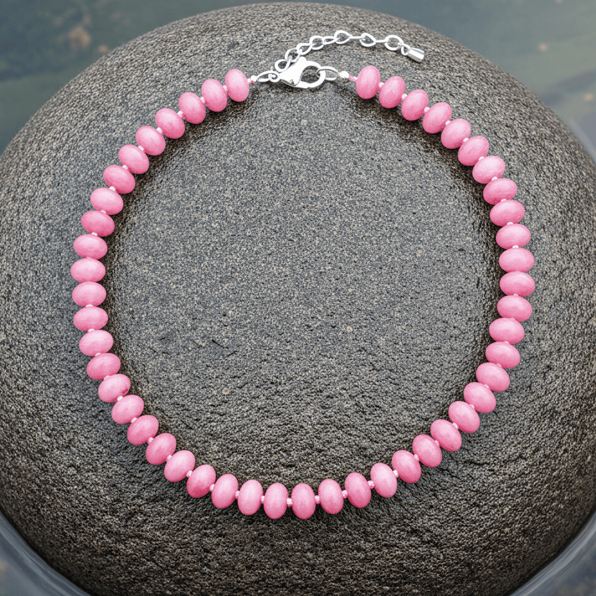 Donker roze handgeknoopte edelstenen ketting met sterling zilver (925) liggend op steen in water | Cherry Quartz Rondelle