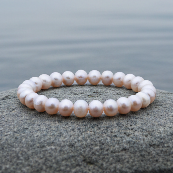 Roze zoetwaterparel armband liggend op steen aan waterrand, elastisch | Round Pink