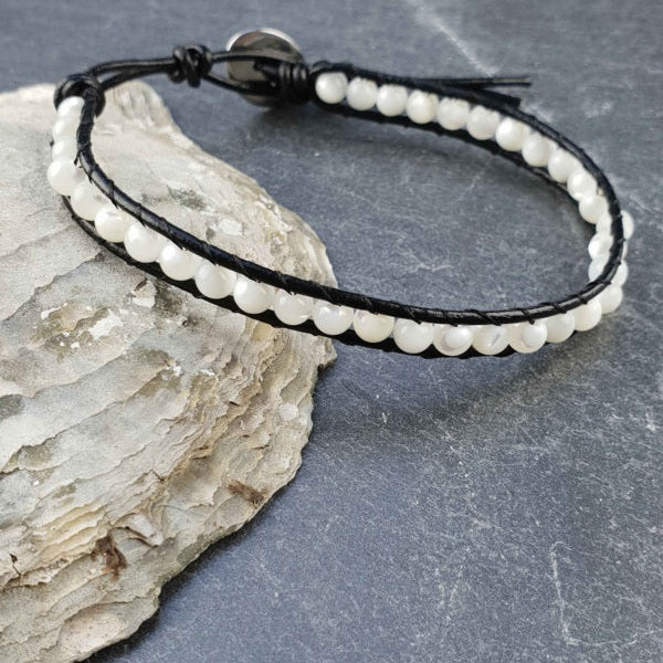 Parelmoeren armband met wit parelmoer en zwart leer liggend tegen schelp | White Shell Wrap