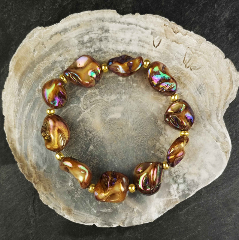 Bruin elastisch parelmoeren armband liggend op witte schelp | Shell AB Brown Gold